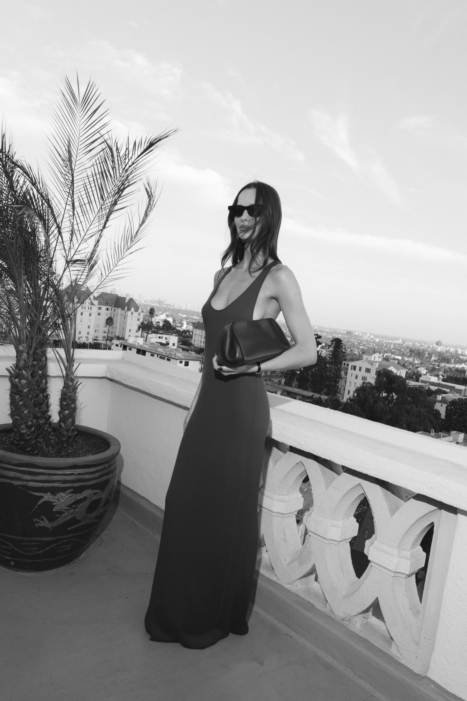 Black and white photo of a rooftop terrace with palm trees and city views.
