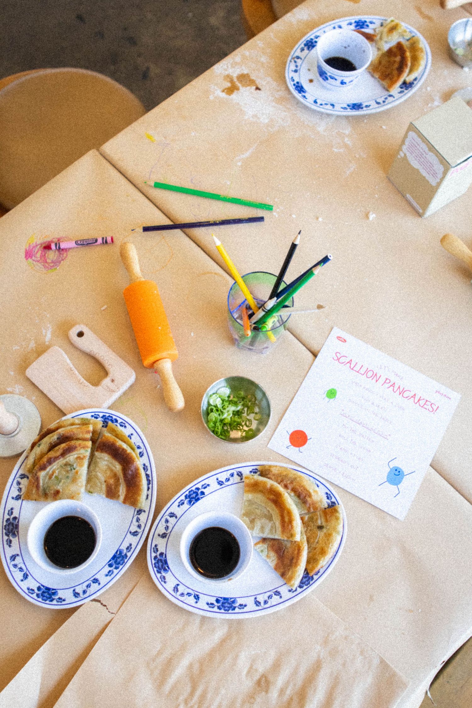 Table setting with Chinese pancakes, tea, and colorful craft supplies.