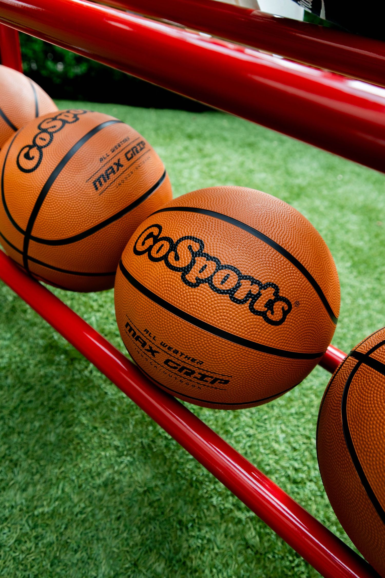 GoSports basketballs lined up on red metal rack with artificial turf background.