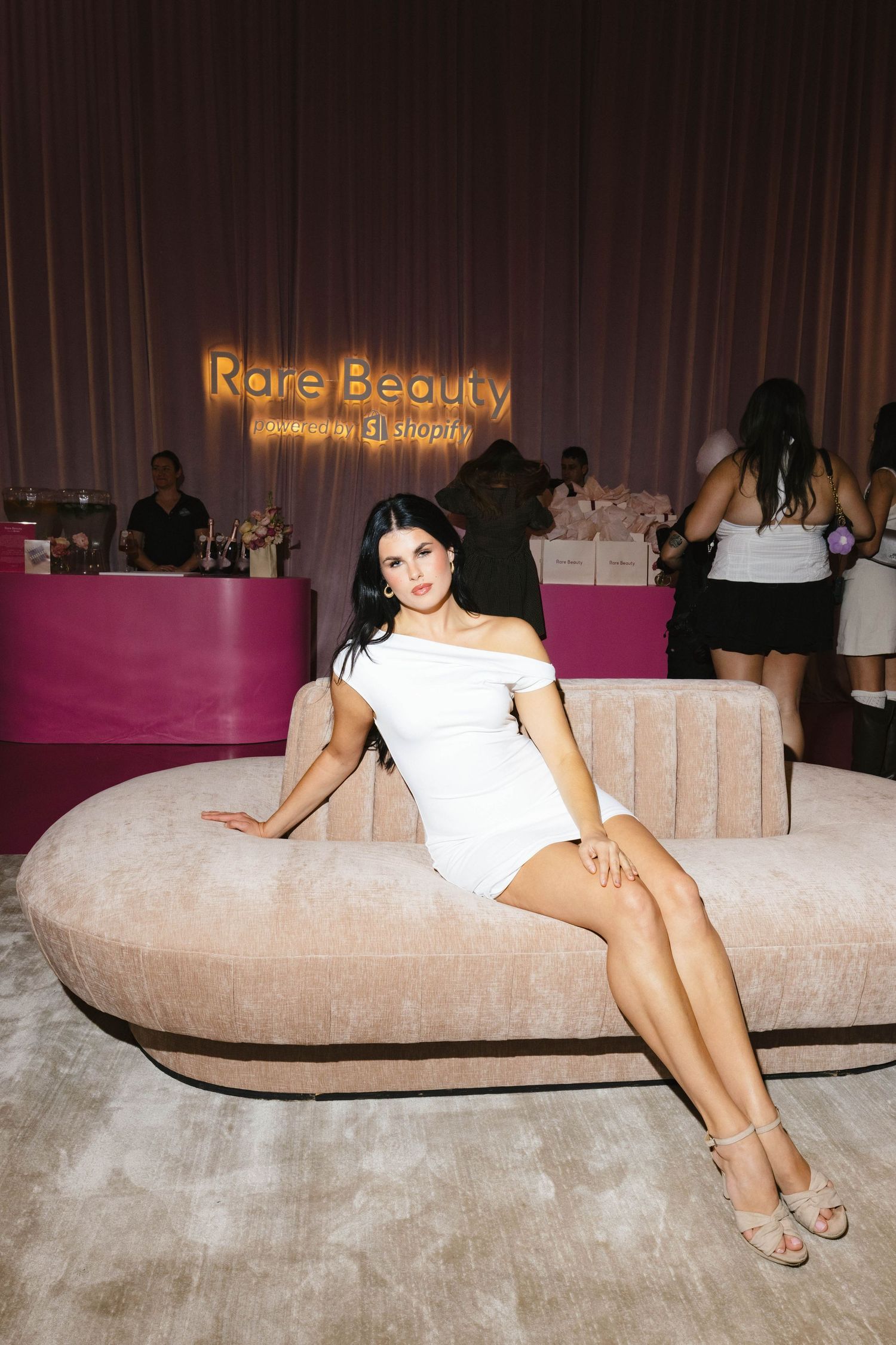 Modern curved beige sofa with illuminated Rare Beauty signage in a pink-toned retail space.