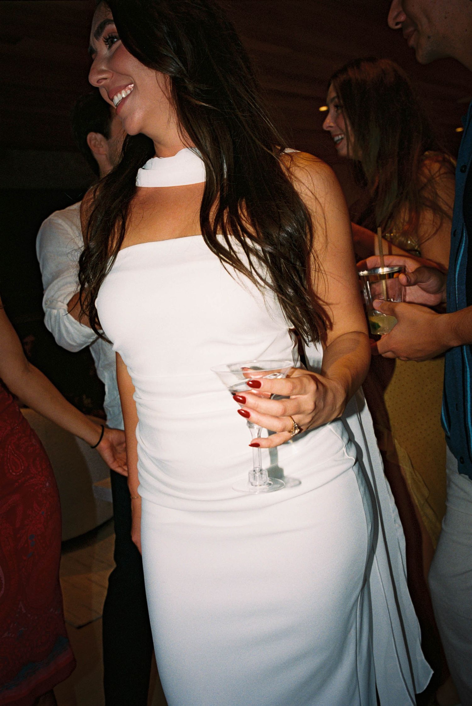 Person in white dress holding cocktail glass at celebration event.