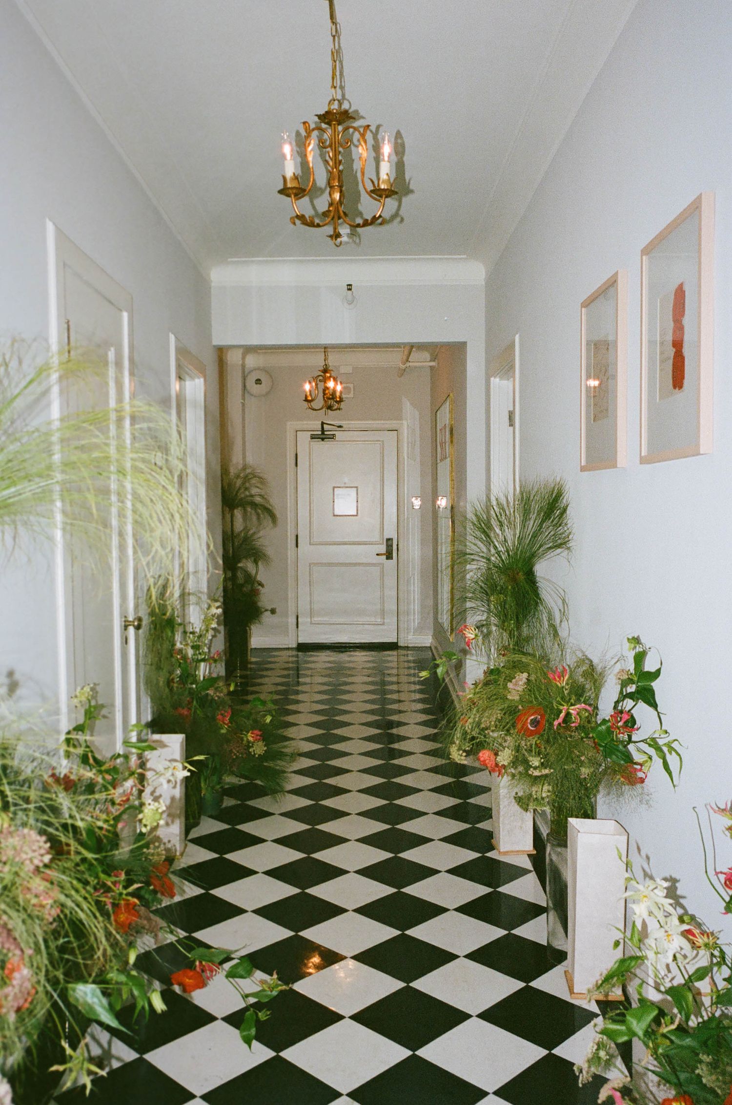 Long corridor with black and white checkerboard flooring and hanging chandeliers.