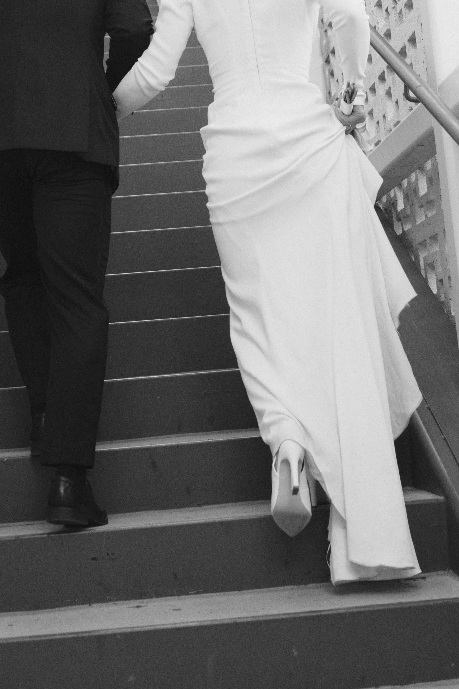 Black and white photo showing elegant white wedding dress details on stairs.