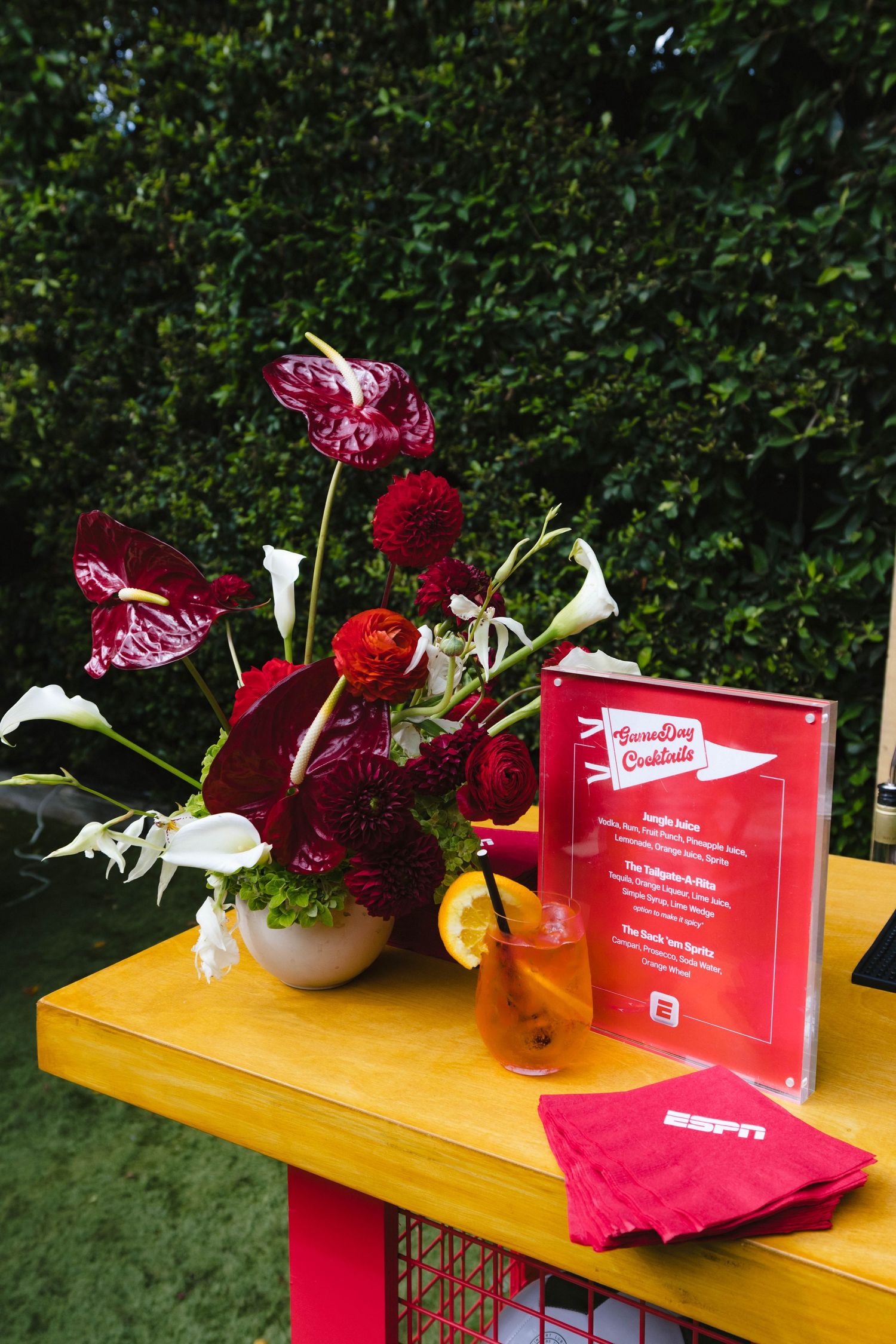 Red floral arrangements and event signage on yellow wooden display table.
