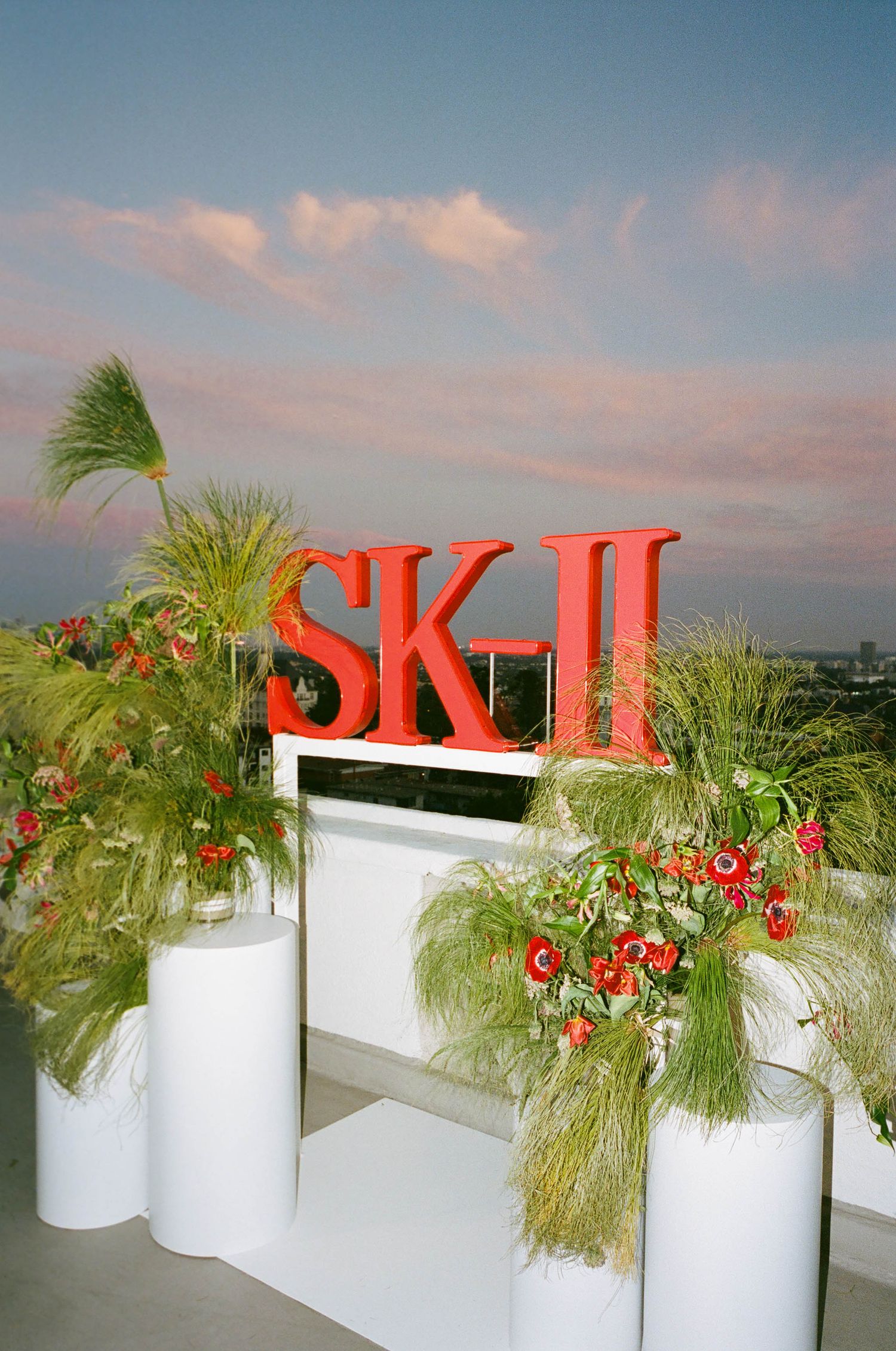 Red SK-II signage displayed on white planters with tropical plants and flowers.