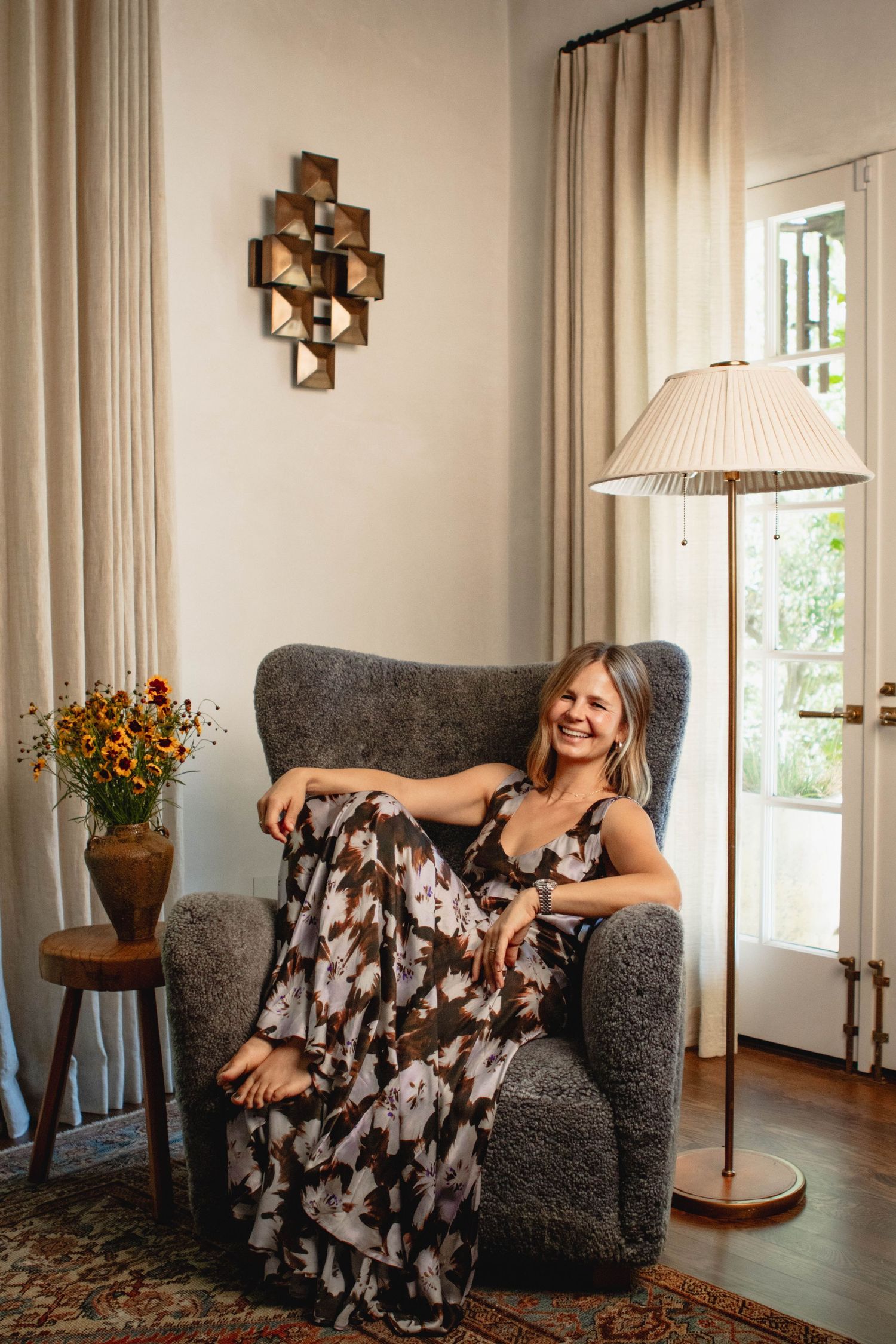 Woman in patterned dress relaxing in grey armchair in elegantly decorated room.