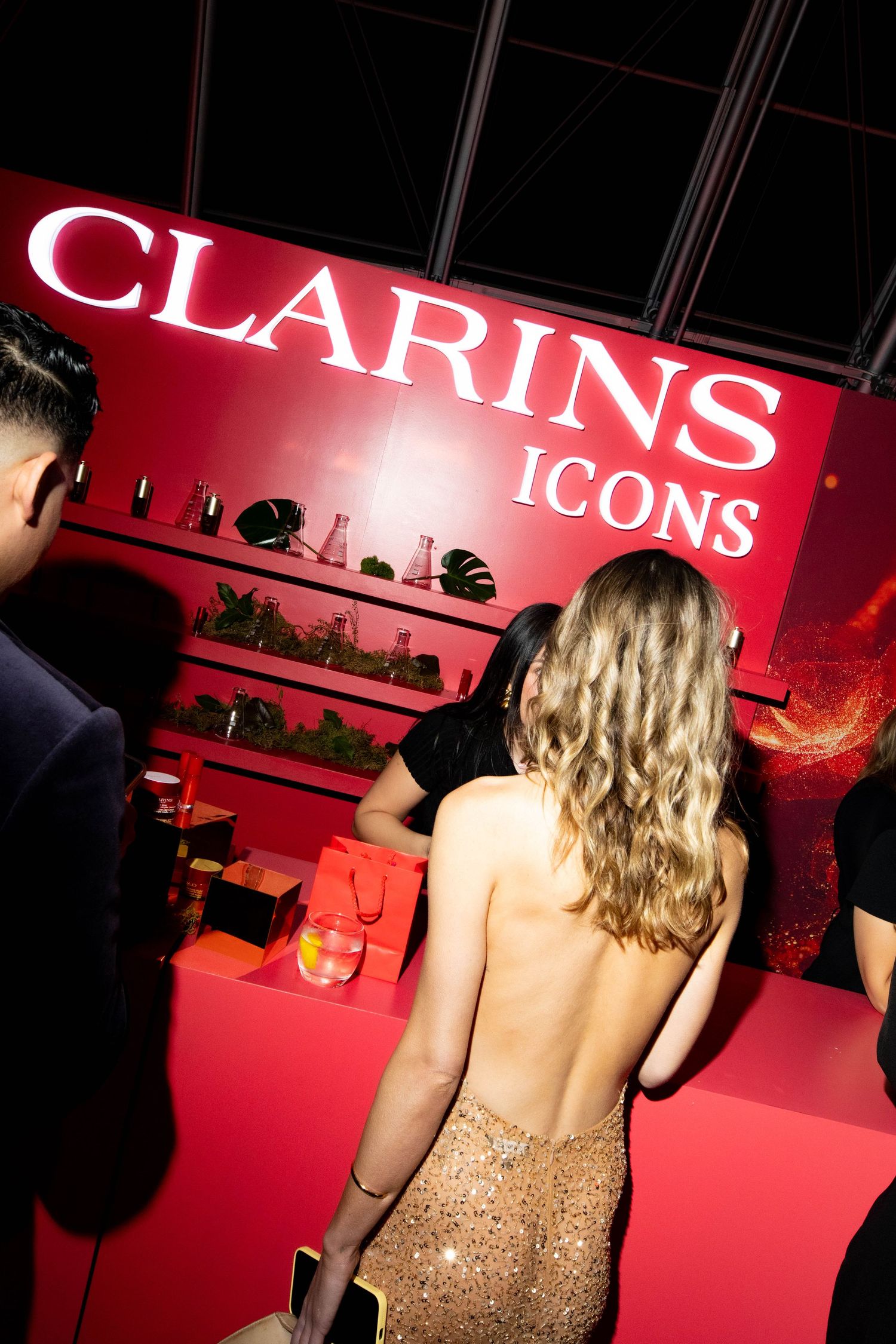 Glamorous Clarins Icons display with red backdrop and beauty products on shelving.