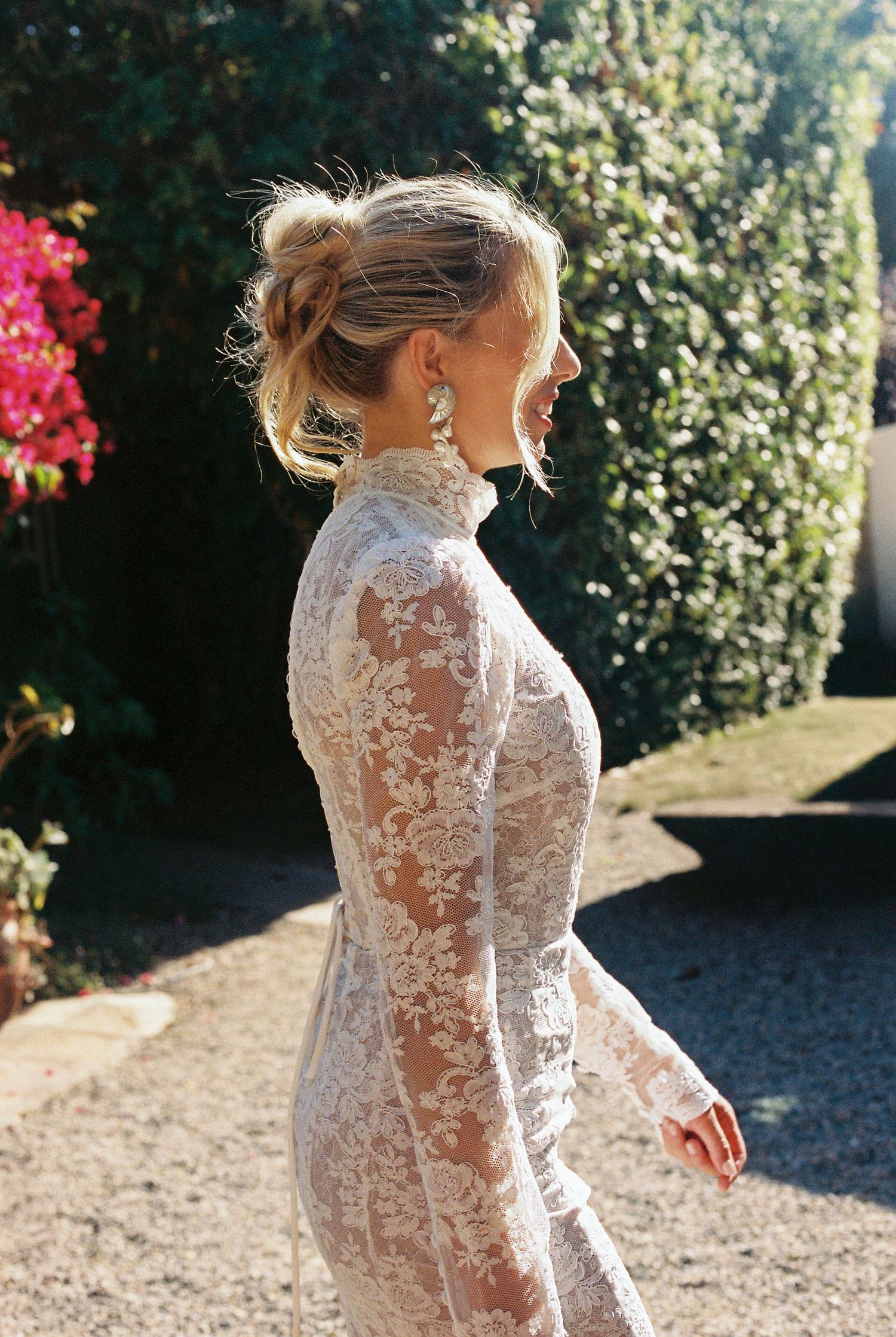 Close-up of a delicate white lace wedding dress with long sleeves against a garden backdrop.
