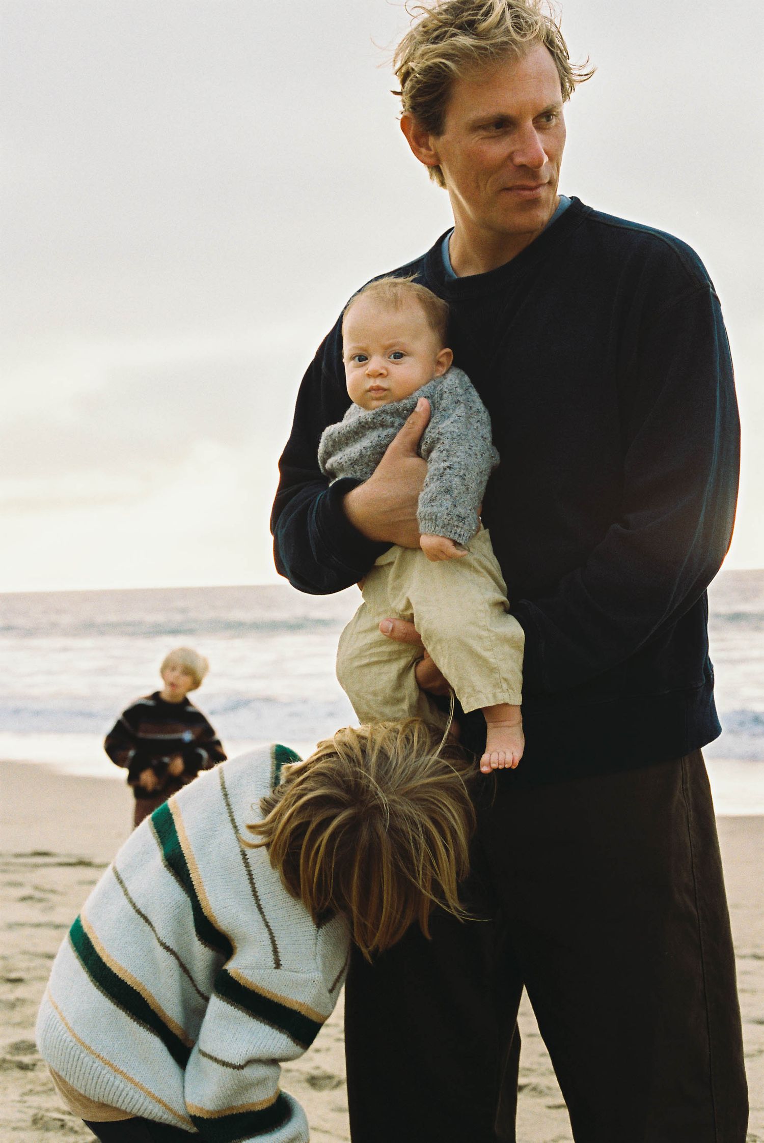 Family members interacting and holding children on a beach during golden hour.