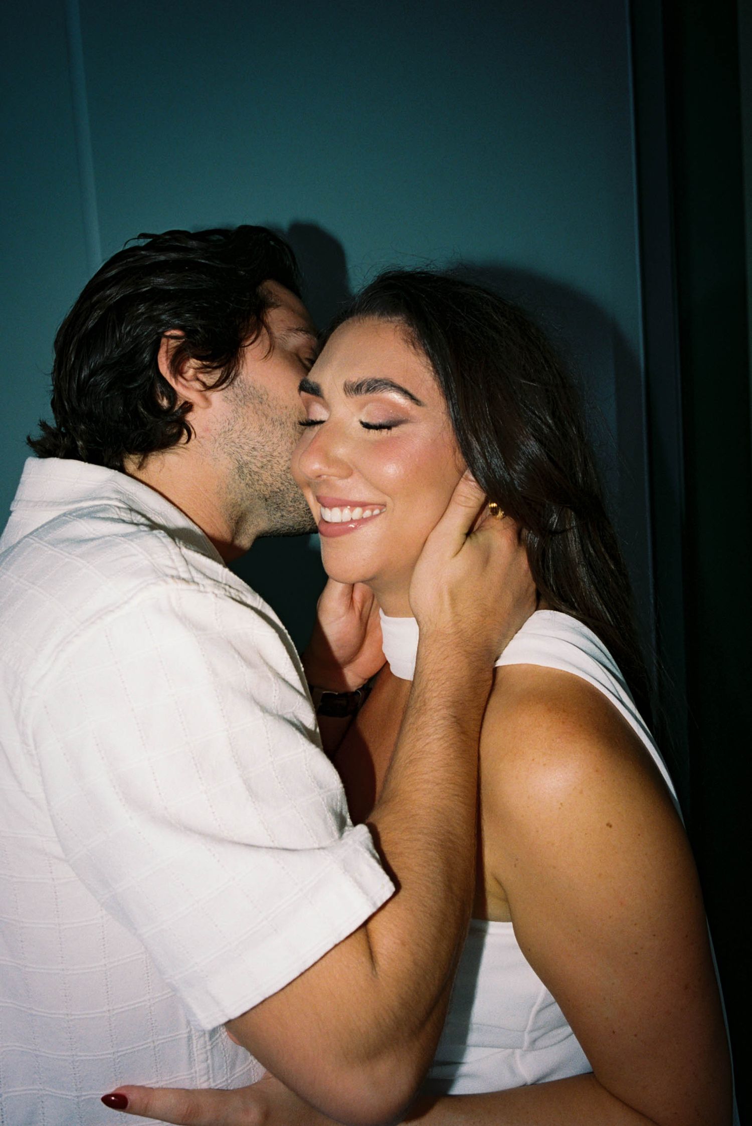 Intimate moment captured between couple against dark teal background.