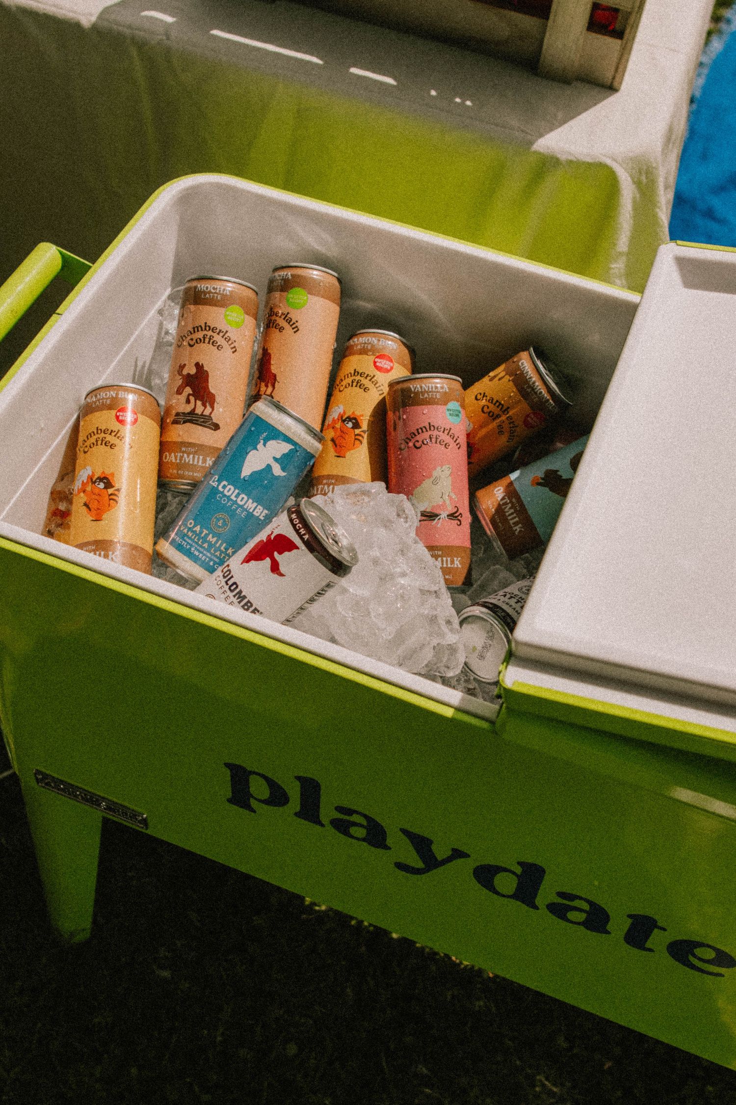 Canned beverages chilling in ice inside a green Playdate branded cooler.