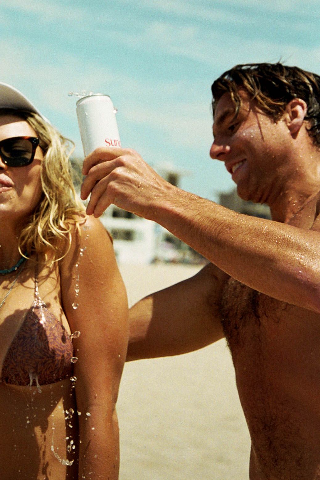Couple playfully splashing water at each other on a sunny beach.