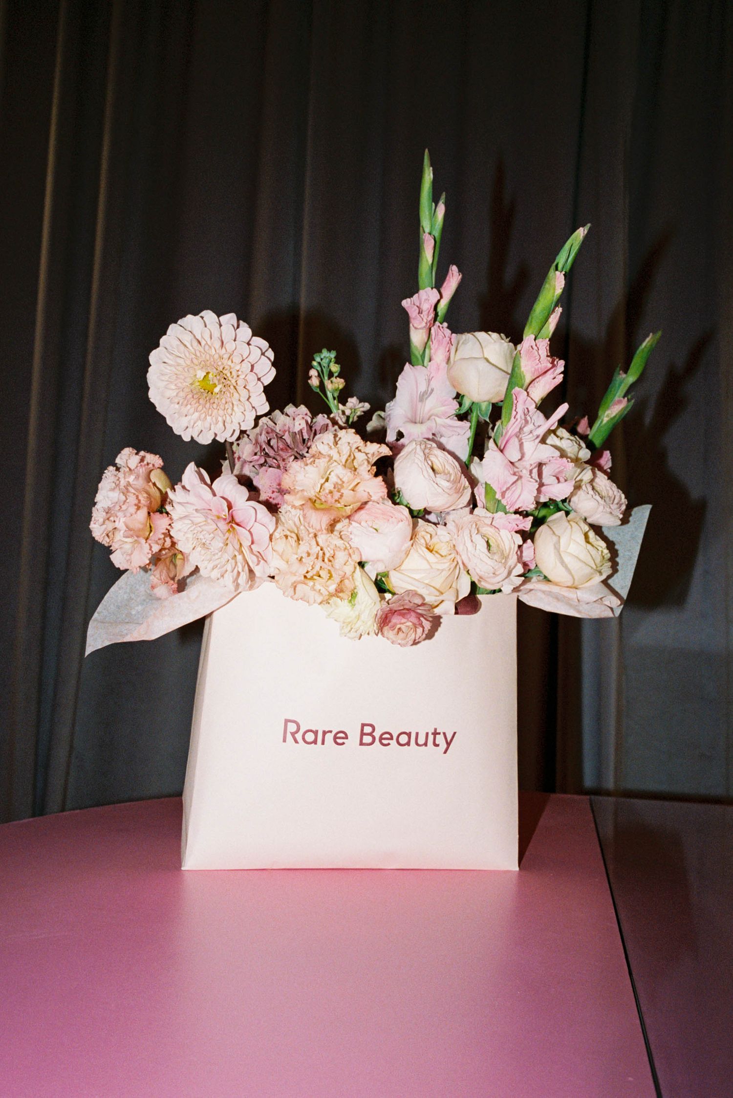 A sequence of pink and peach floral arrangements in white vases against a dark background with text reading 'Rare Beauty'.