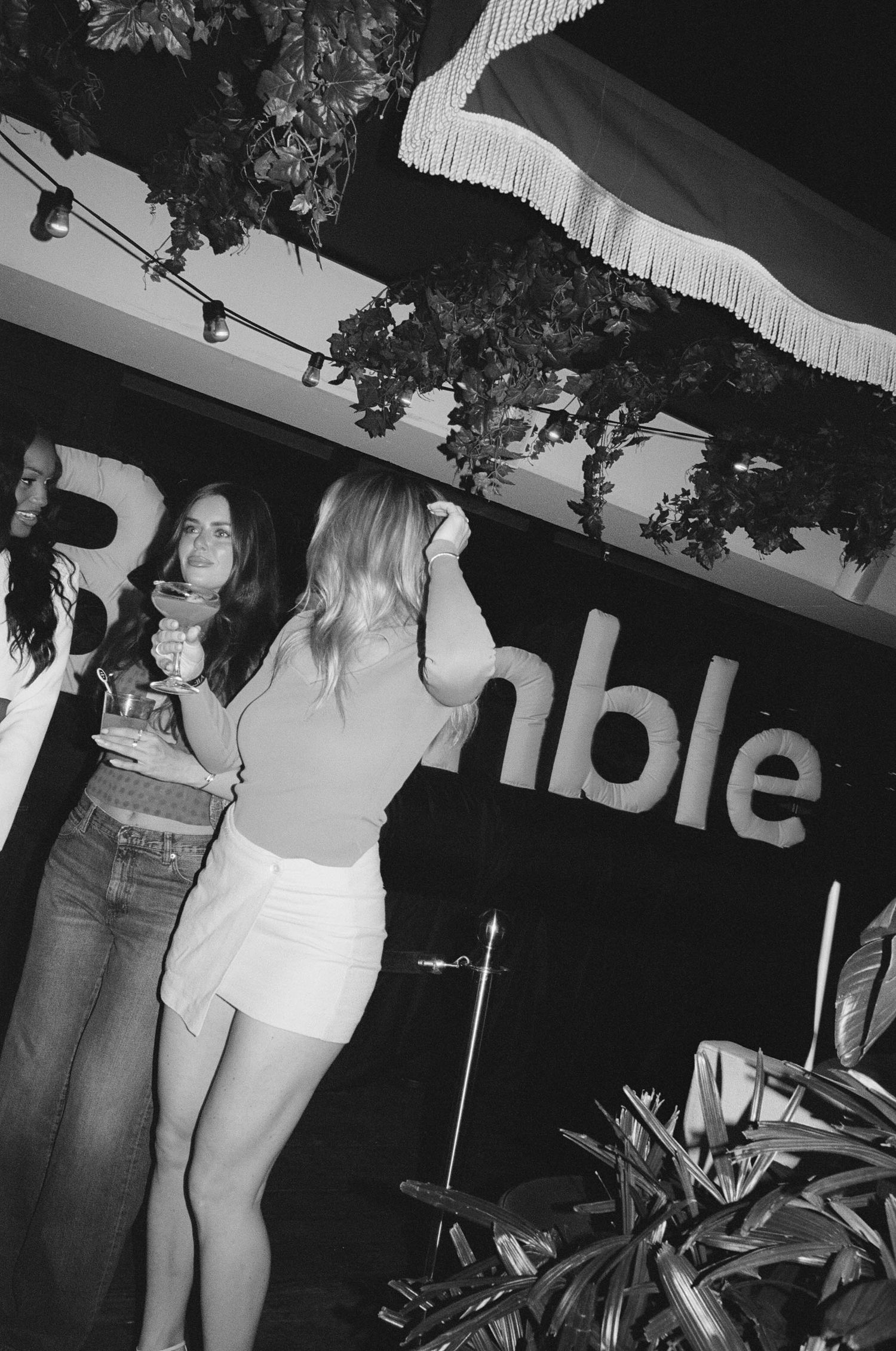 Black and white photo of women dancing at a Bumble event, with tropical decor and string lights overhead.