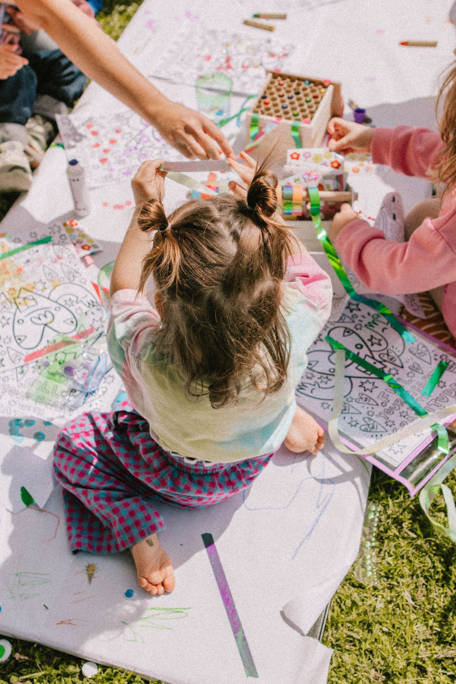 Children coloring and doing creative activities on a blanket outdoors with art supplies and coloring books.