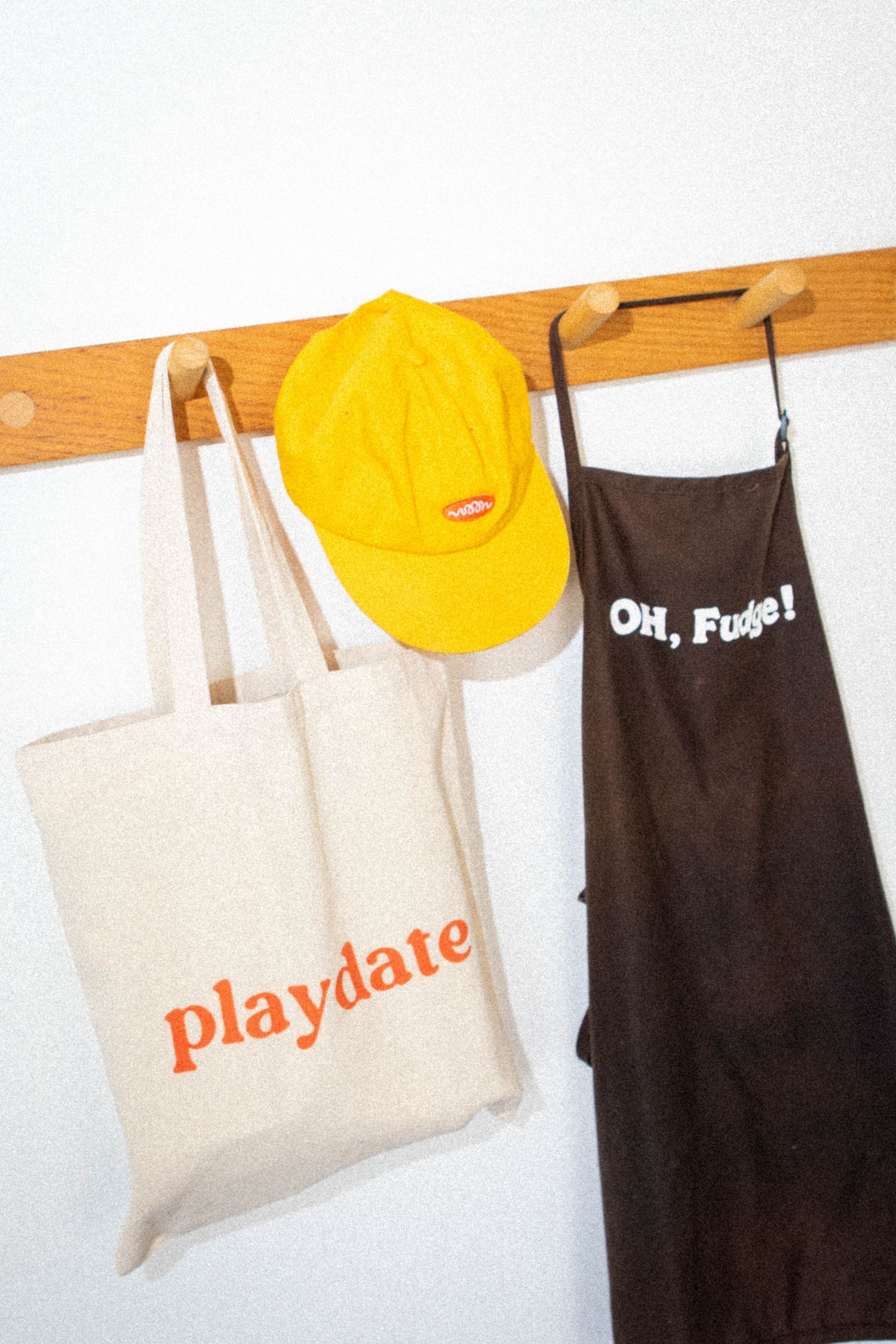 Yellow cap and tote bags hanging on wooden wall hooks with playful text designs.