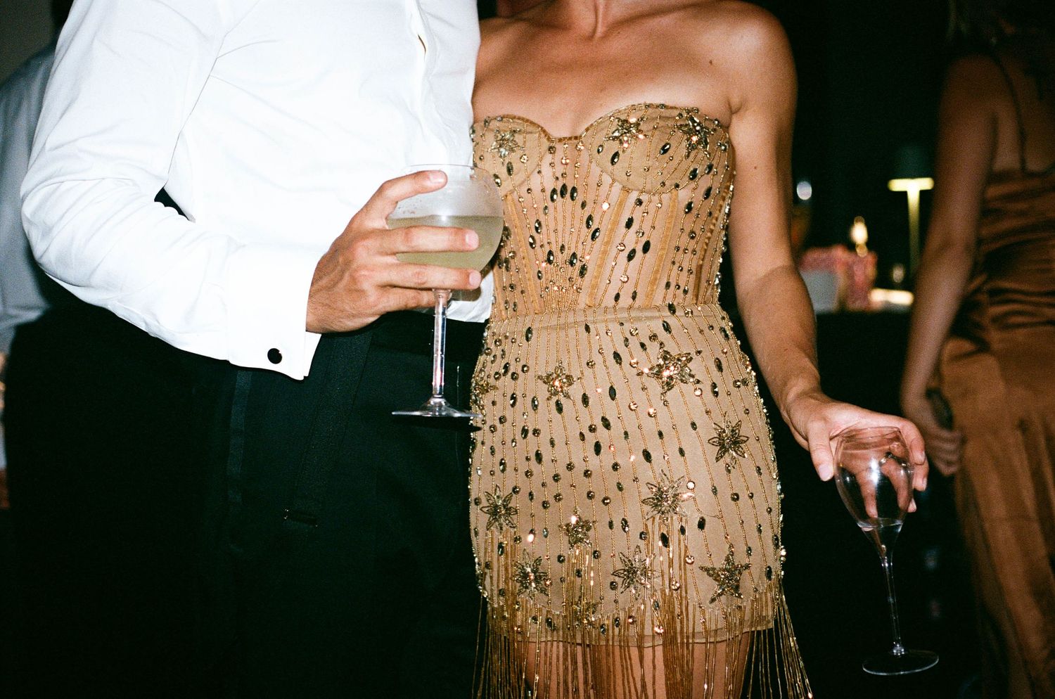 Glamorous evening party scene with sparkly beige dresses and champagne glasses in a dimly lit setting.