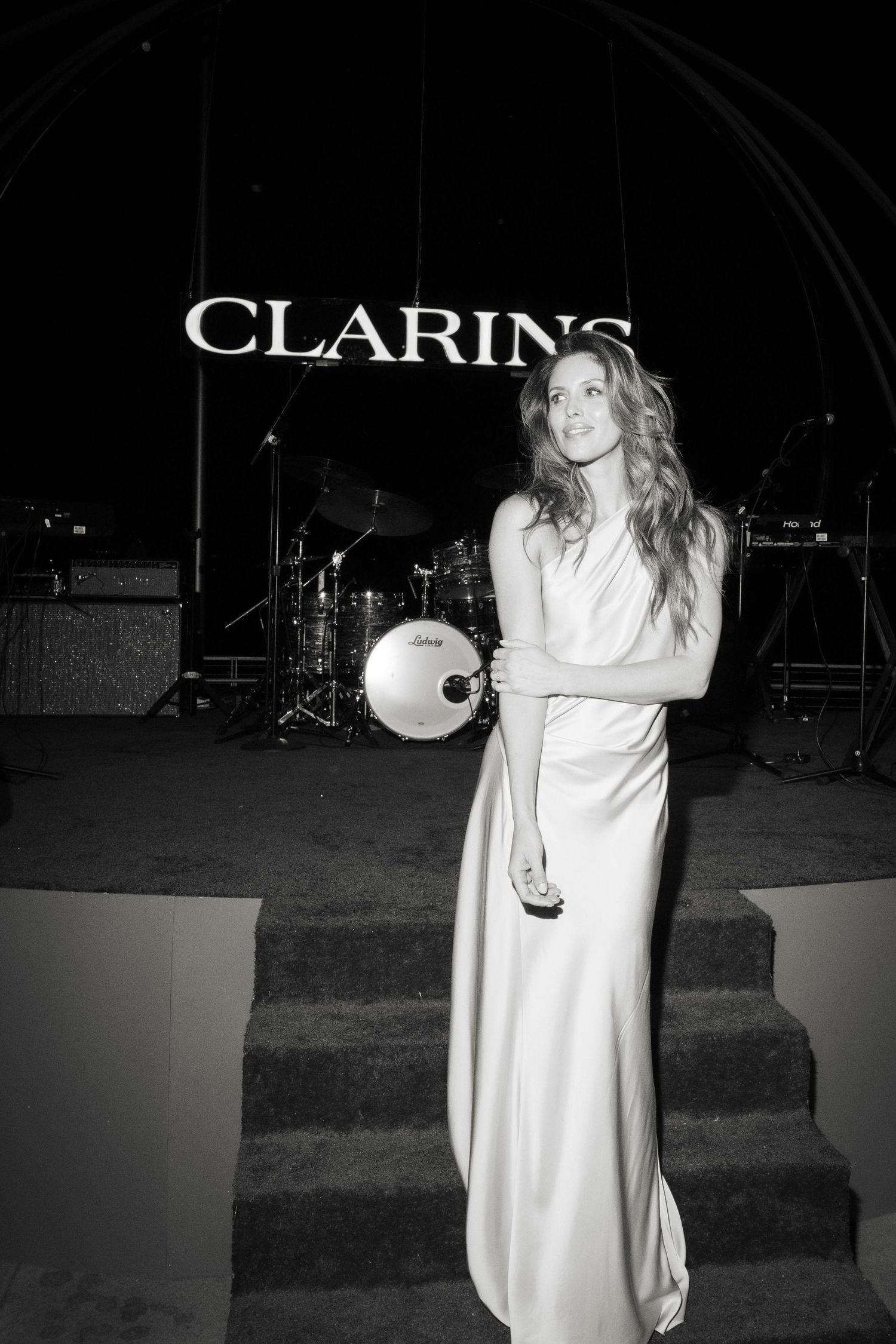 A figure in a flowing white dress stands on dark stage steps in a dramatic black and white photograph.