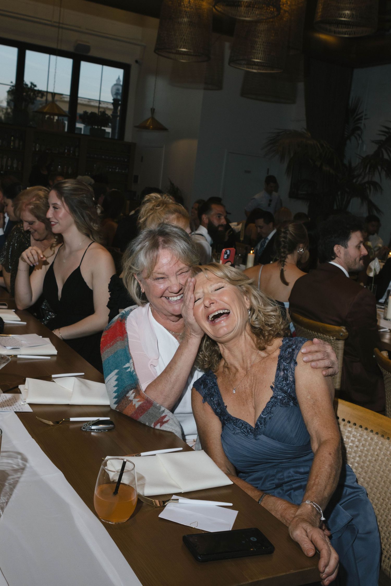 A group of people laughing together while seated at tables during what appears to be a social gathering.