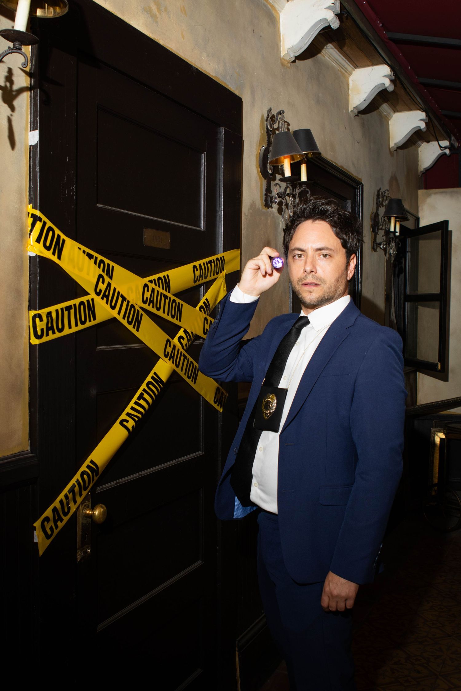 Yellow caution tape stretches across a dark hallway with a person in a blue suit standing behind it.