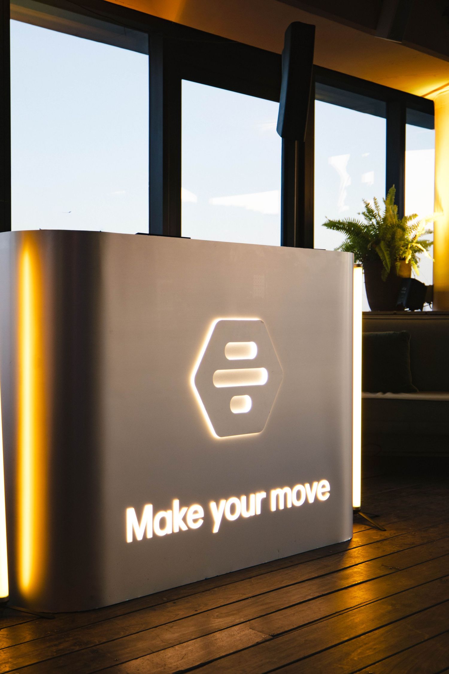 Illuminated reception desk with hexagonal logo and glowing Make your move slogan in modern office interior.