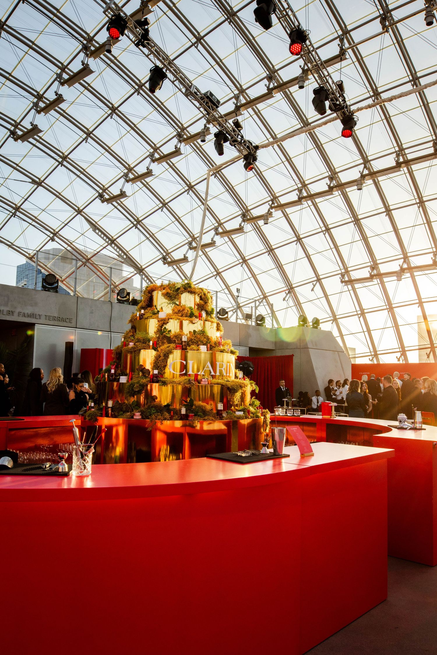 Luxurious event setup with golden tiered display under glass atrium ceiling.