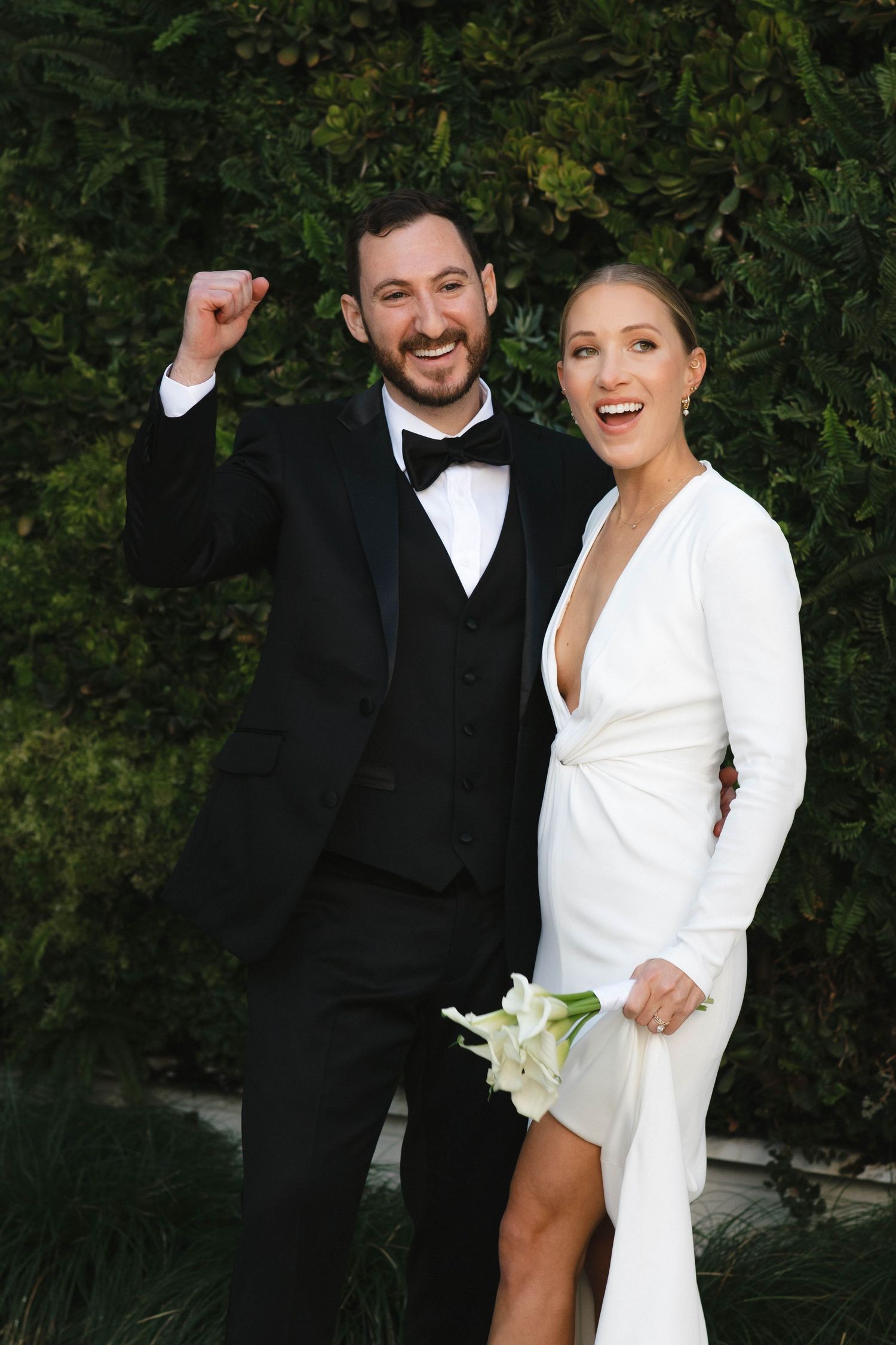 A couple shares a joyful moment in formal black and white attire against a garden backdrop.