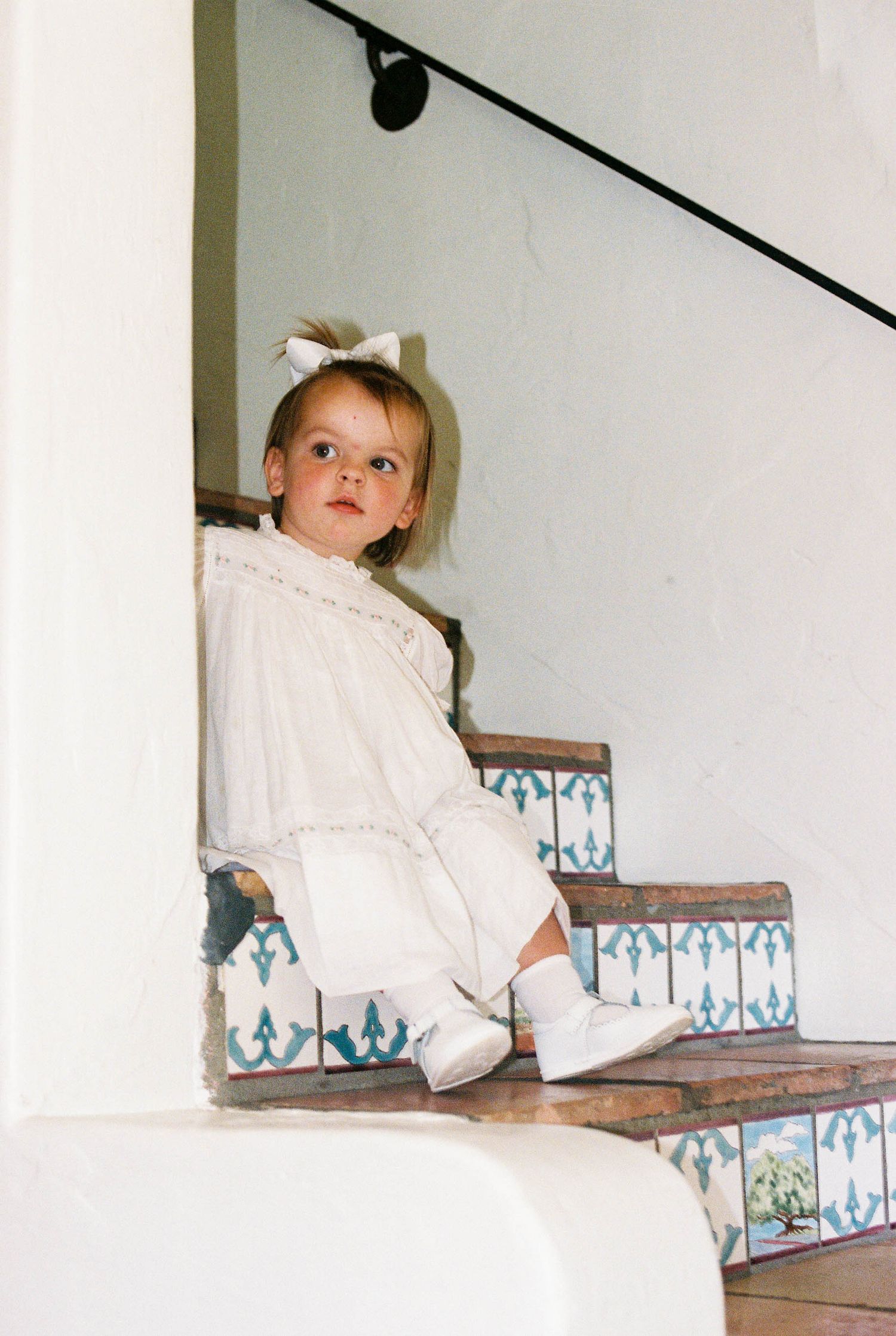 Child in white clothing sitting on decorative tiled stairs.