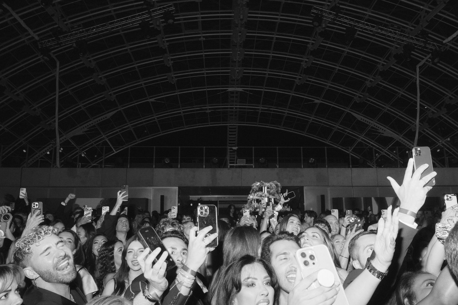 Concert crowd with raised hands silhouetted against dark background during live performance.