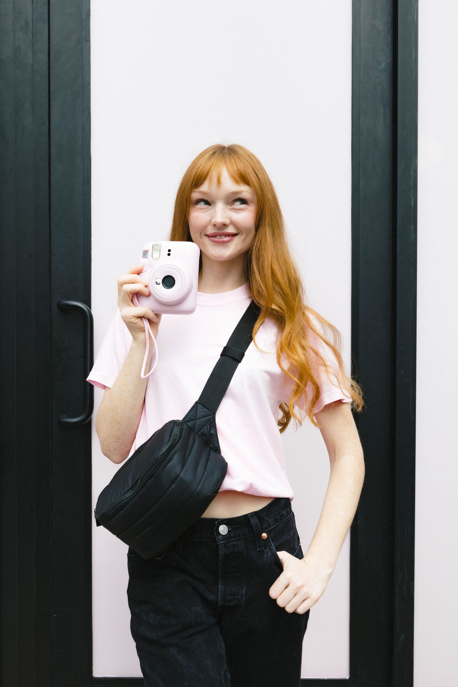 Person wearing black overalls and pink shirt holding a pink camera.