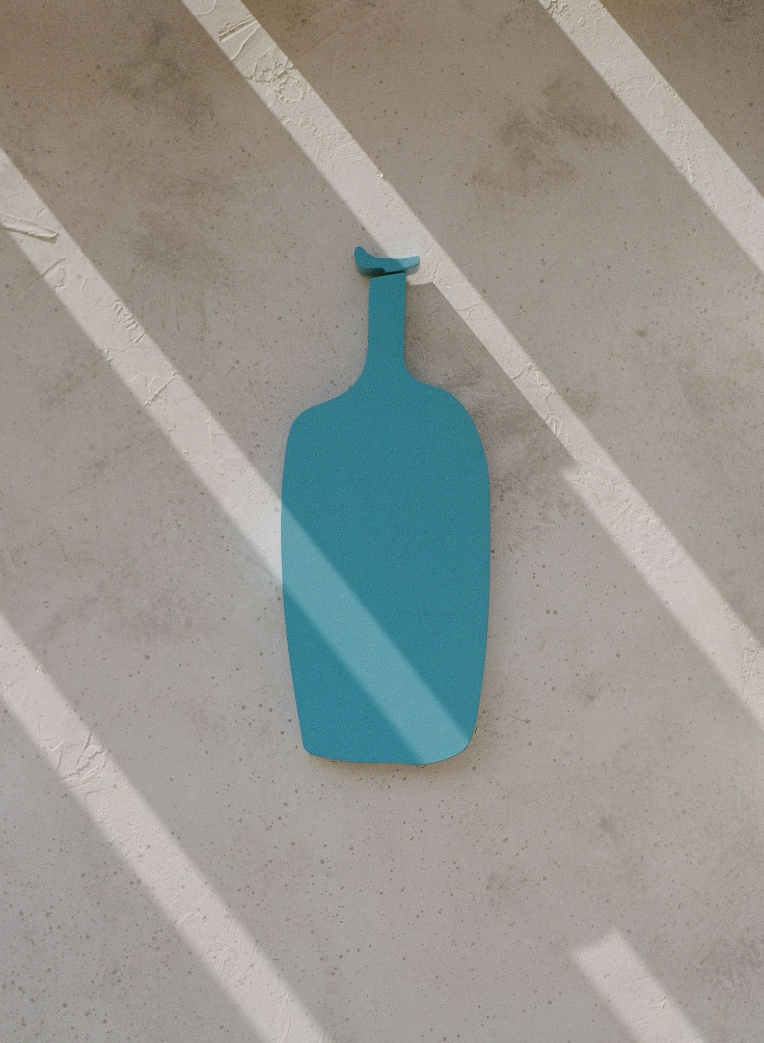 Teal blue bottle-shaped decorative wall mirror hanging on a concrete wall with diagonal light streaks.