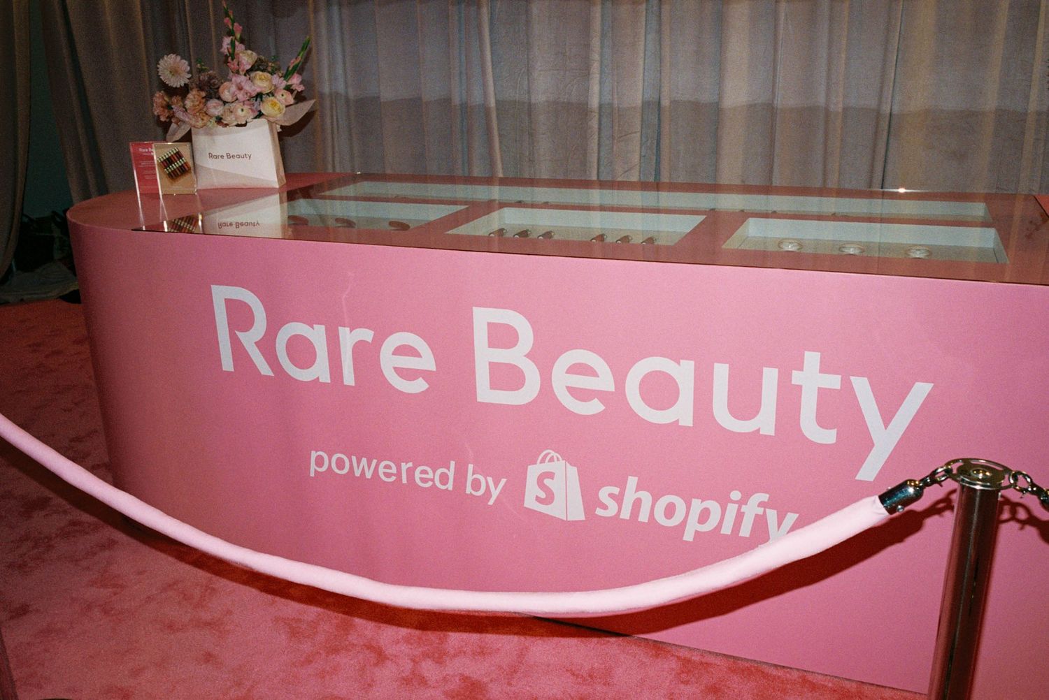 Pink neon signage with 'Rare Beauty' text glows against a wall, powered by Shopify.