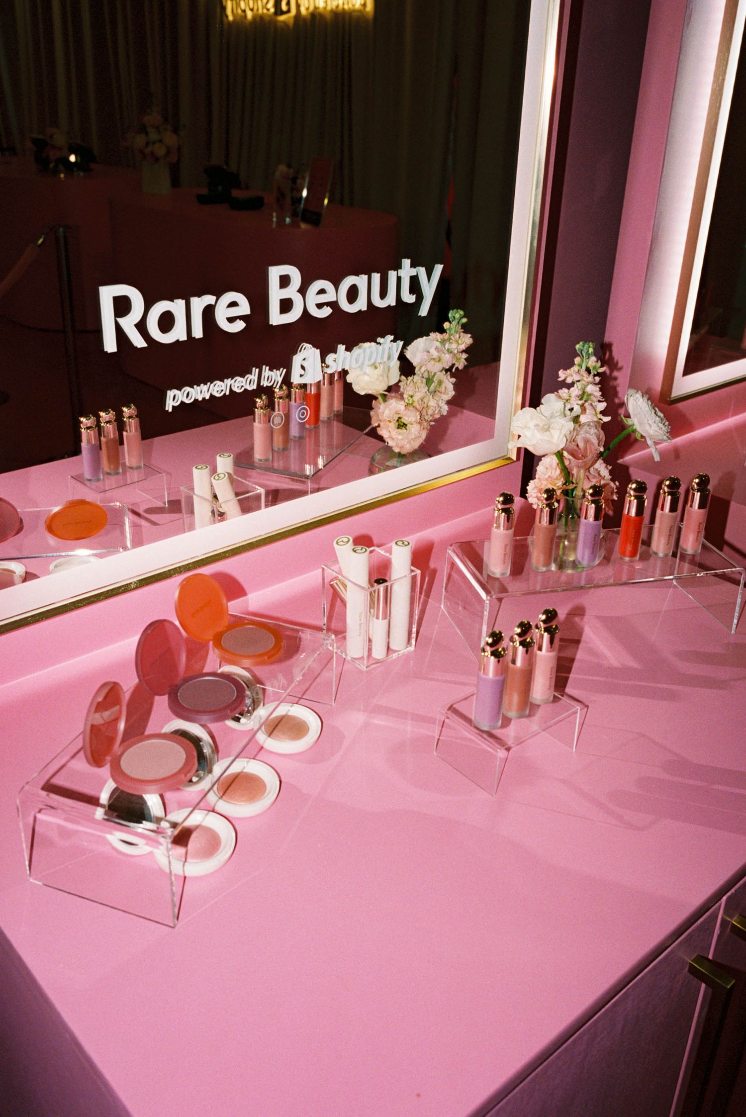 Pink-themed beauty product display with Rare Beauty branding and cosmetic testers.