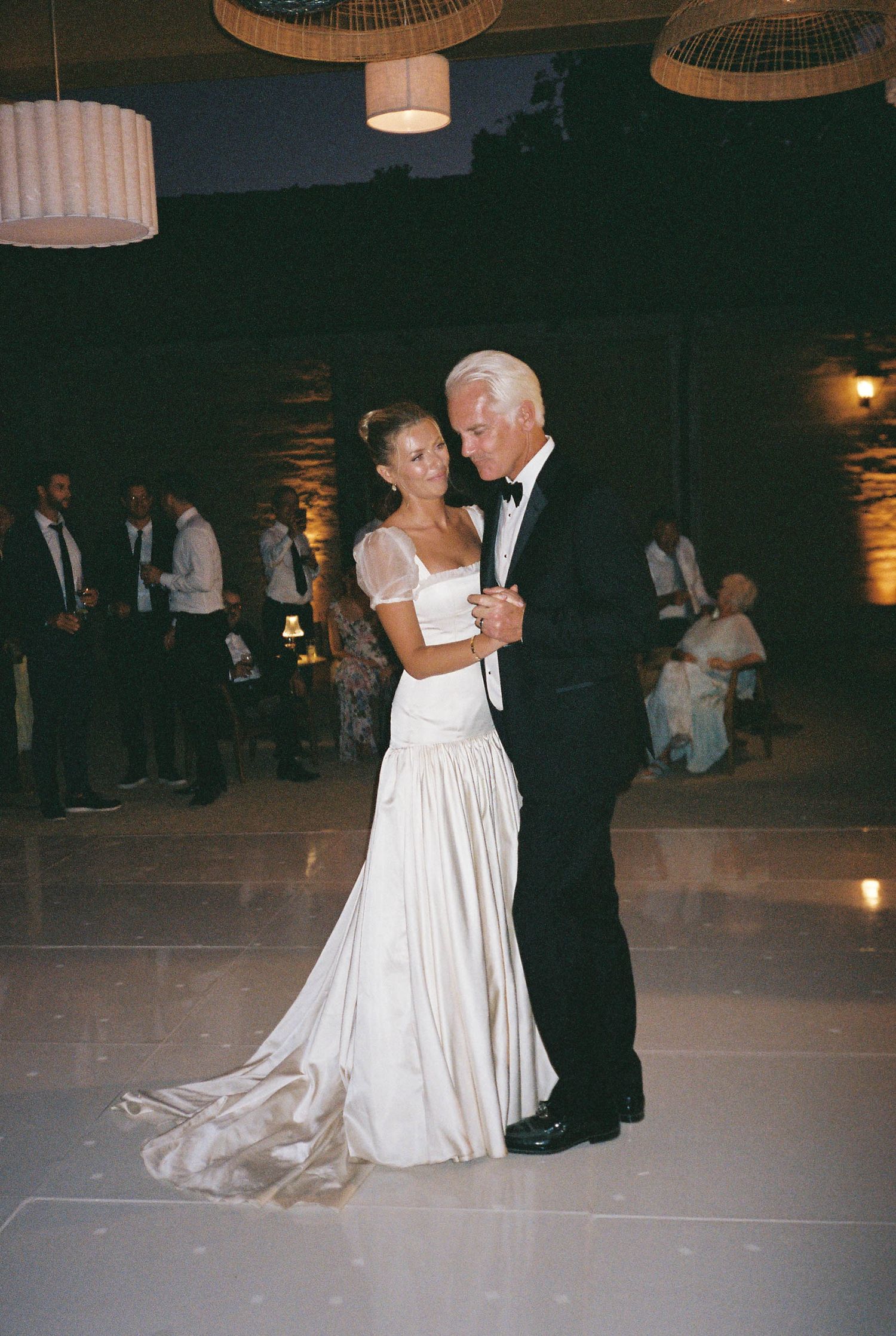 Couple dancing under woven pendant lights at an evening wedding reception.