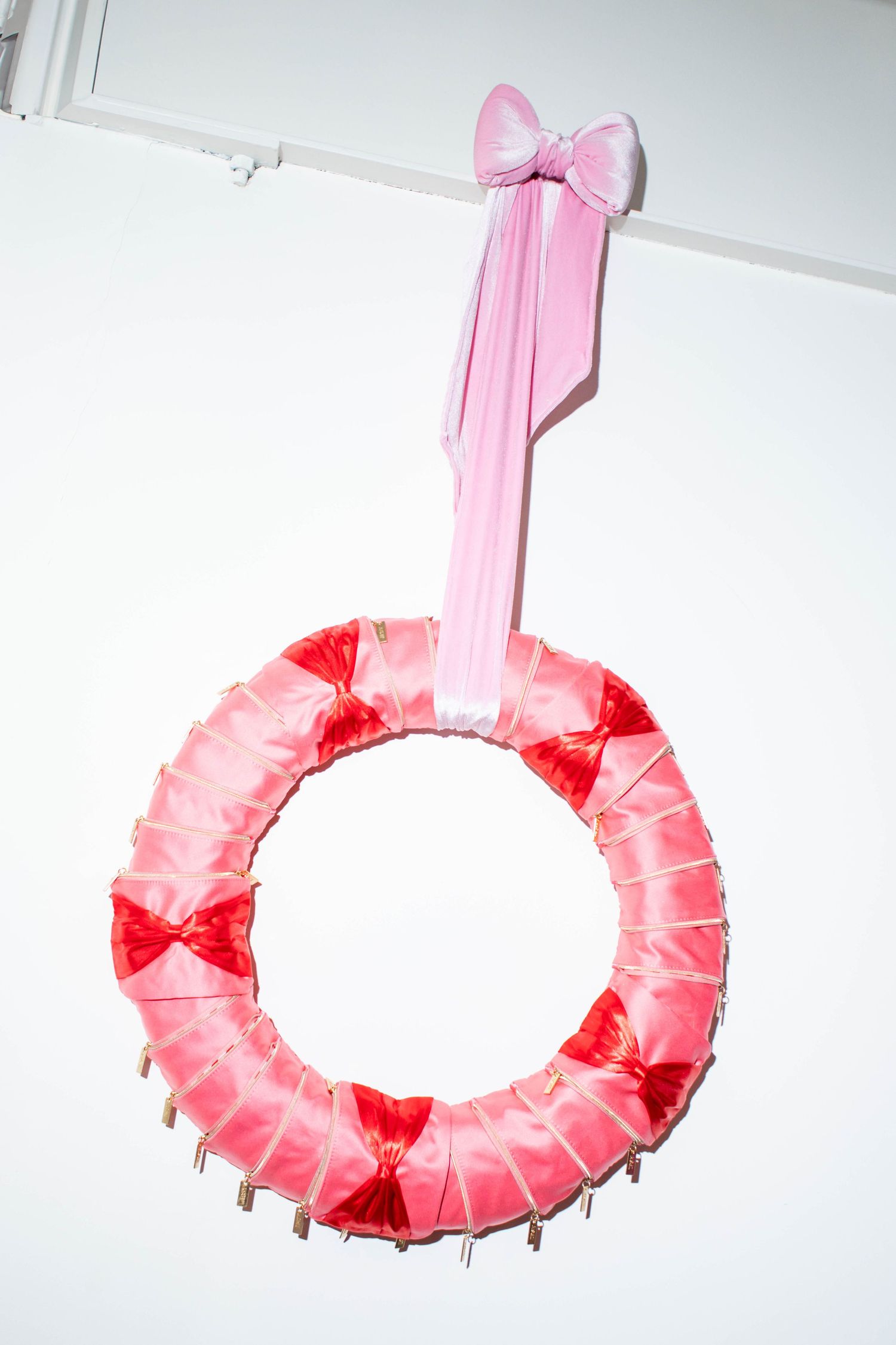 Pink decorative wreath with bow hanging against white background.