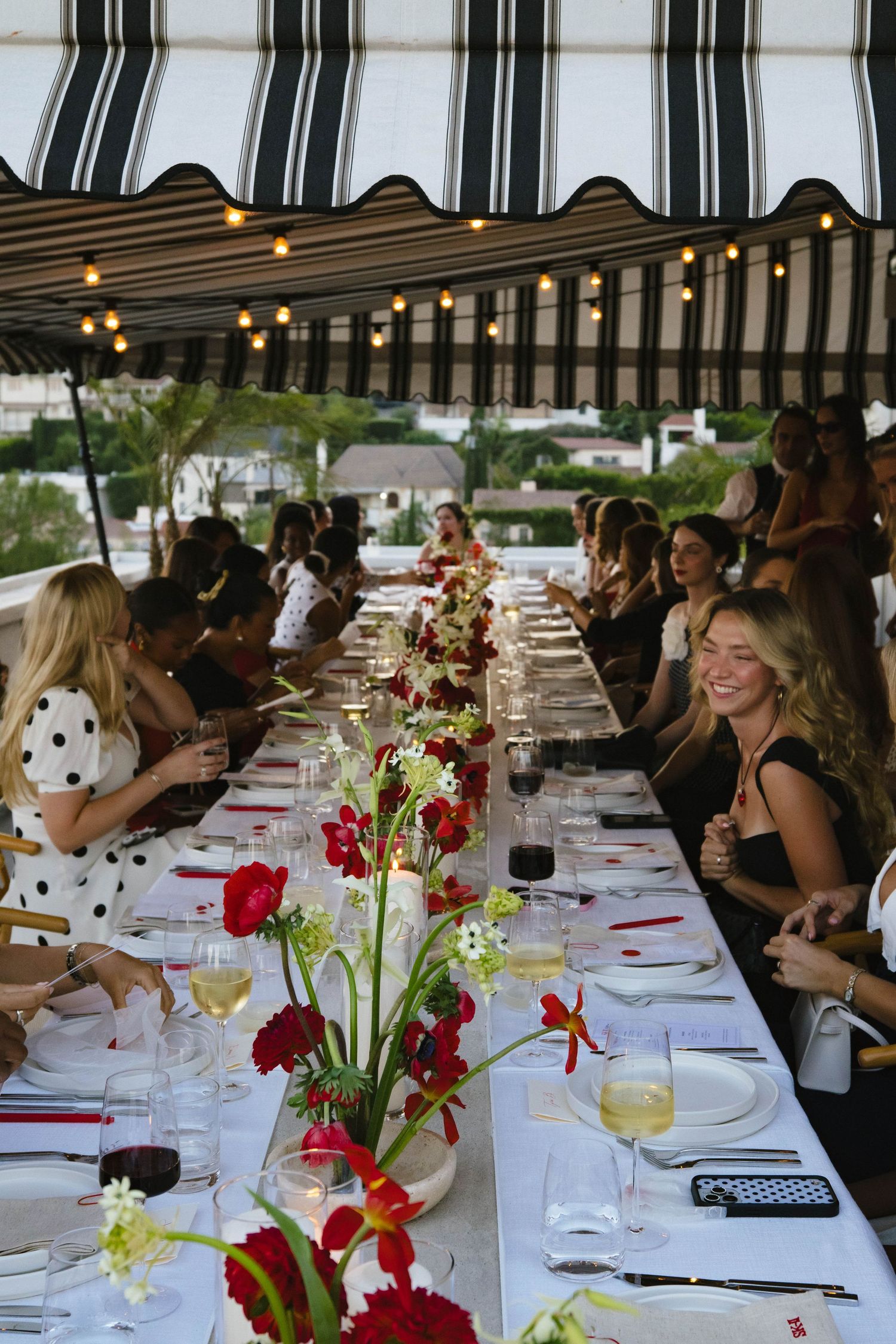 Elegant dinner party with floral centerpieces and striped awning overhead.