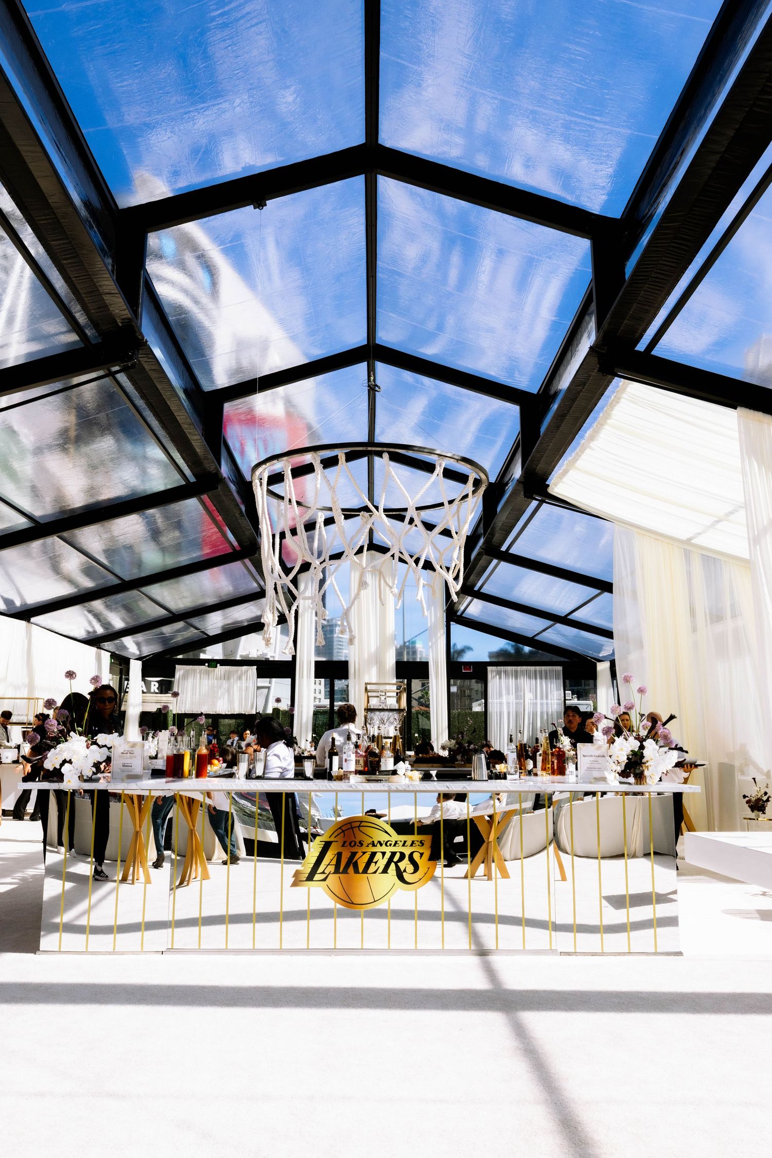 LA Lakers themed bar under glass ceiling with basketball hoop chandelier and gold team logo display.