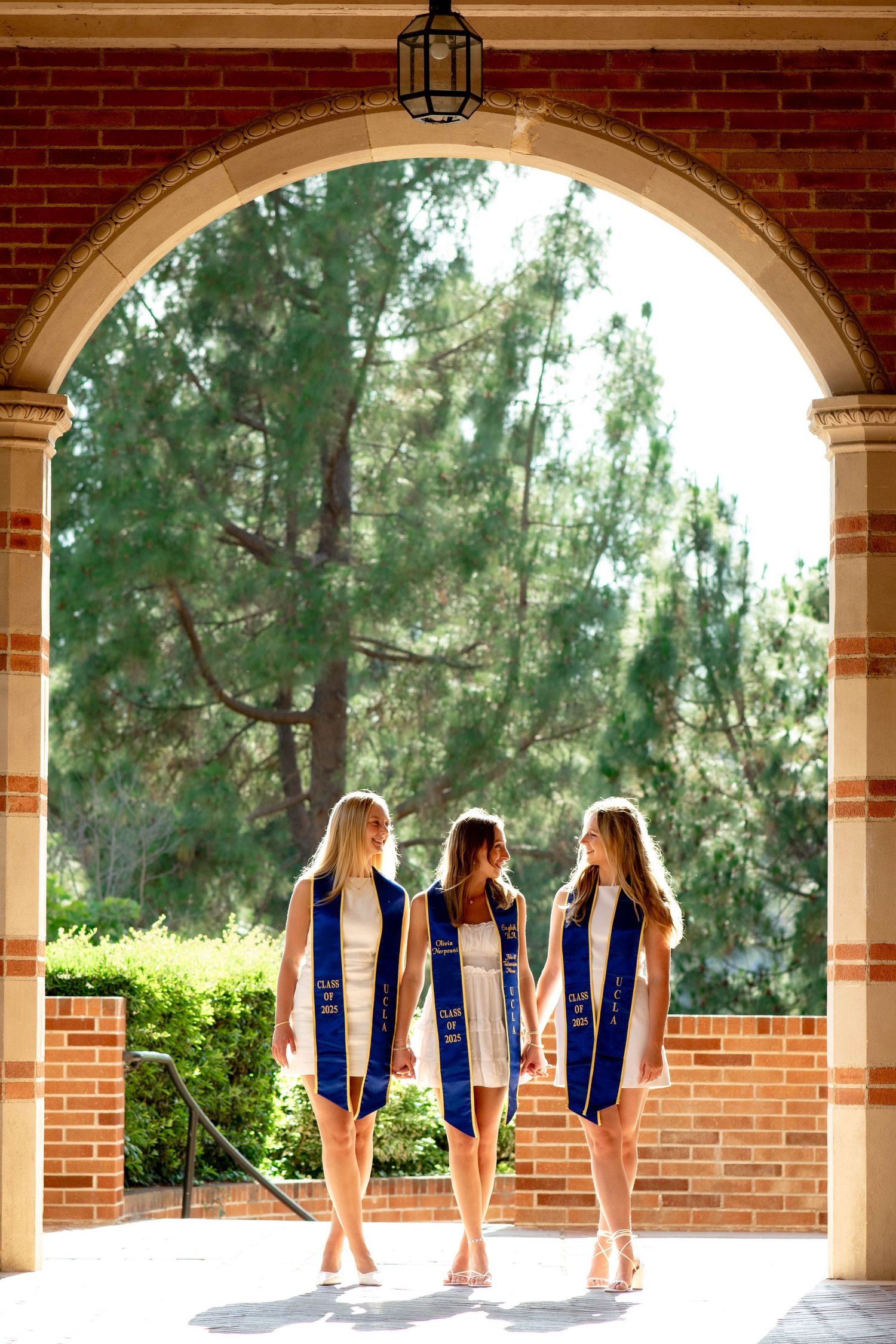 Group of friends in matching navy blue dresses pose together under arched brick walkway on sunny day.
