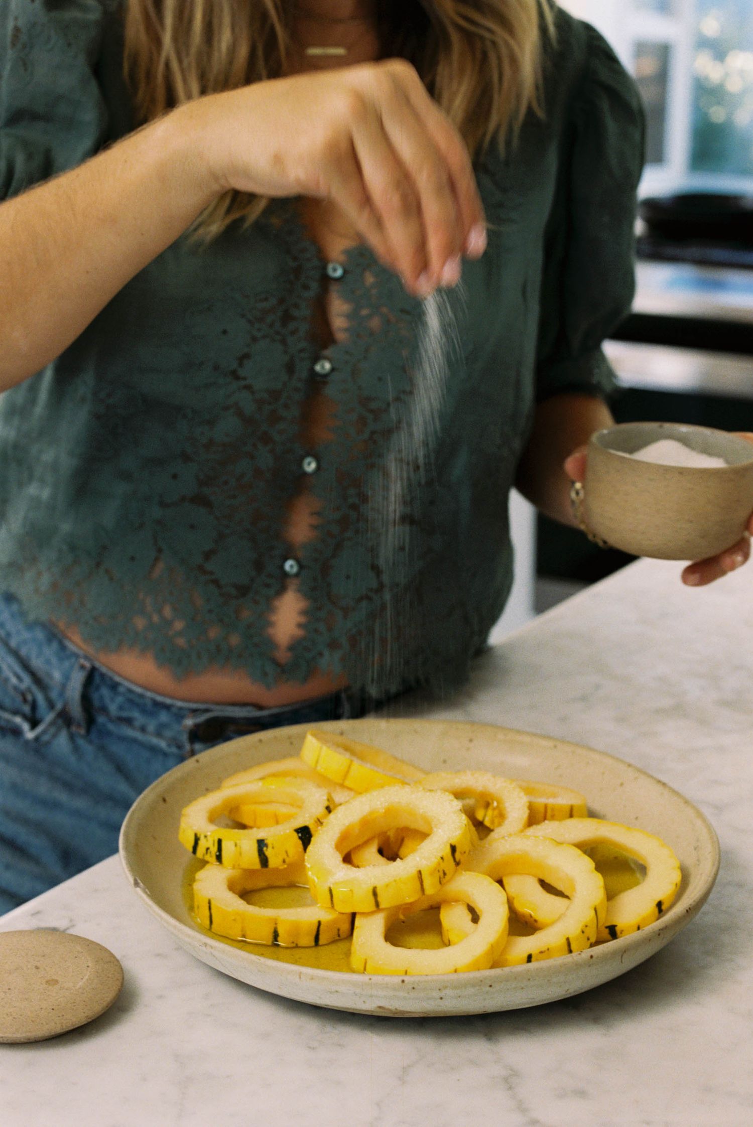 Sliced yellow delicata squash arranged on a white plate with hands preparing the dish.