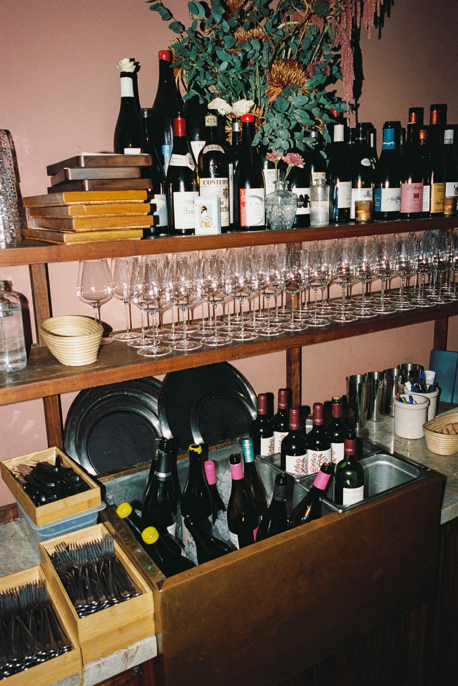 Wine storage shelves filled with bottles and glasses in organized rows.