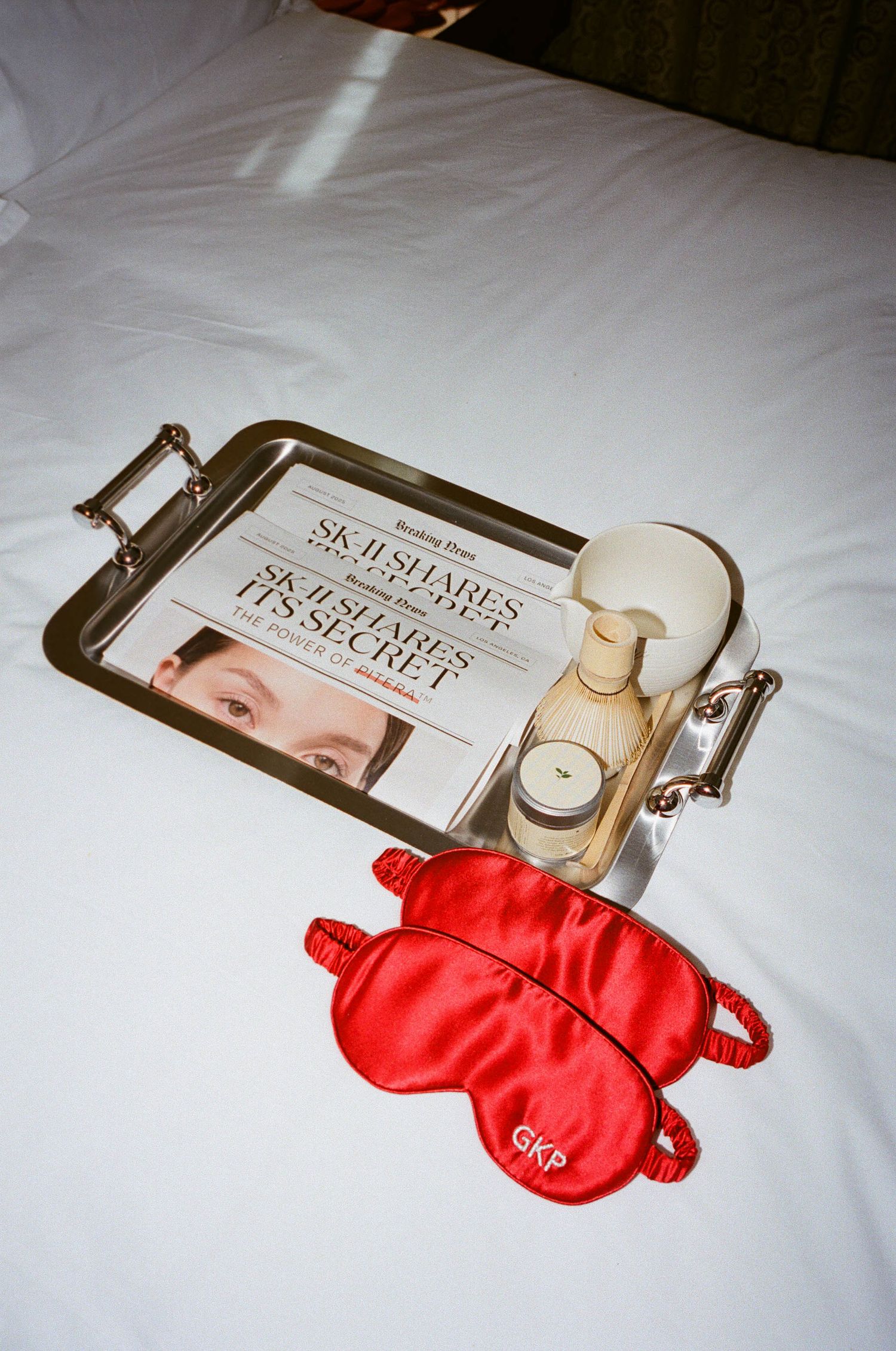 Red sleep mask and magazine displayed on white bedding.