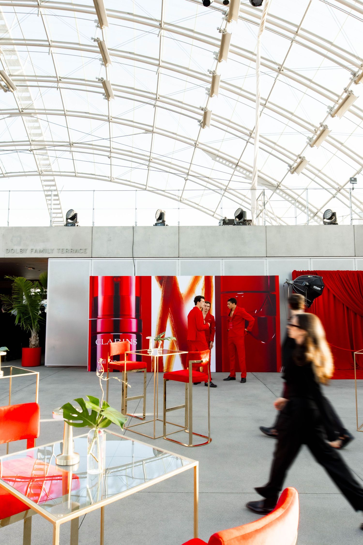 Modern exhibition space with glass ceiling, red accents, and display pedestals arranged in a geometric pattern.
