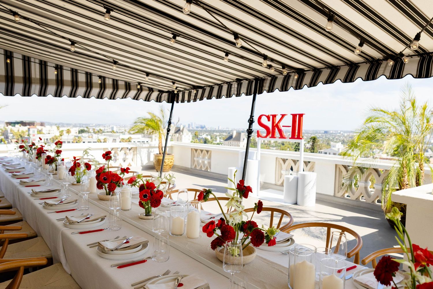 Elegant outdoor dining setup with striped awning and red floral centerpieces.