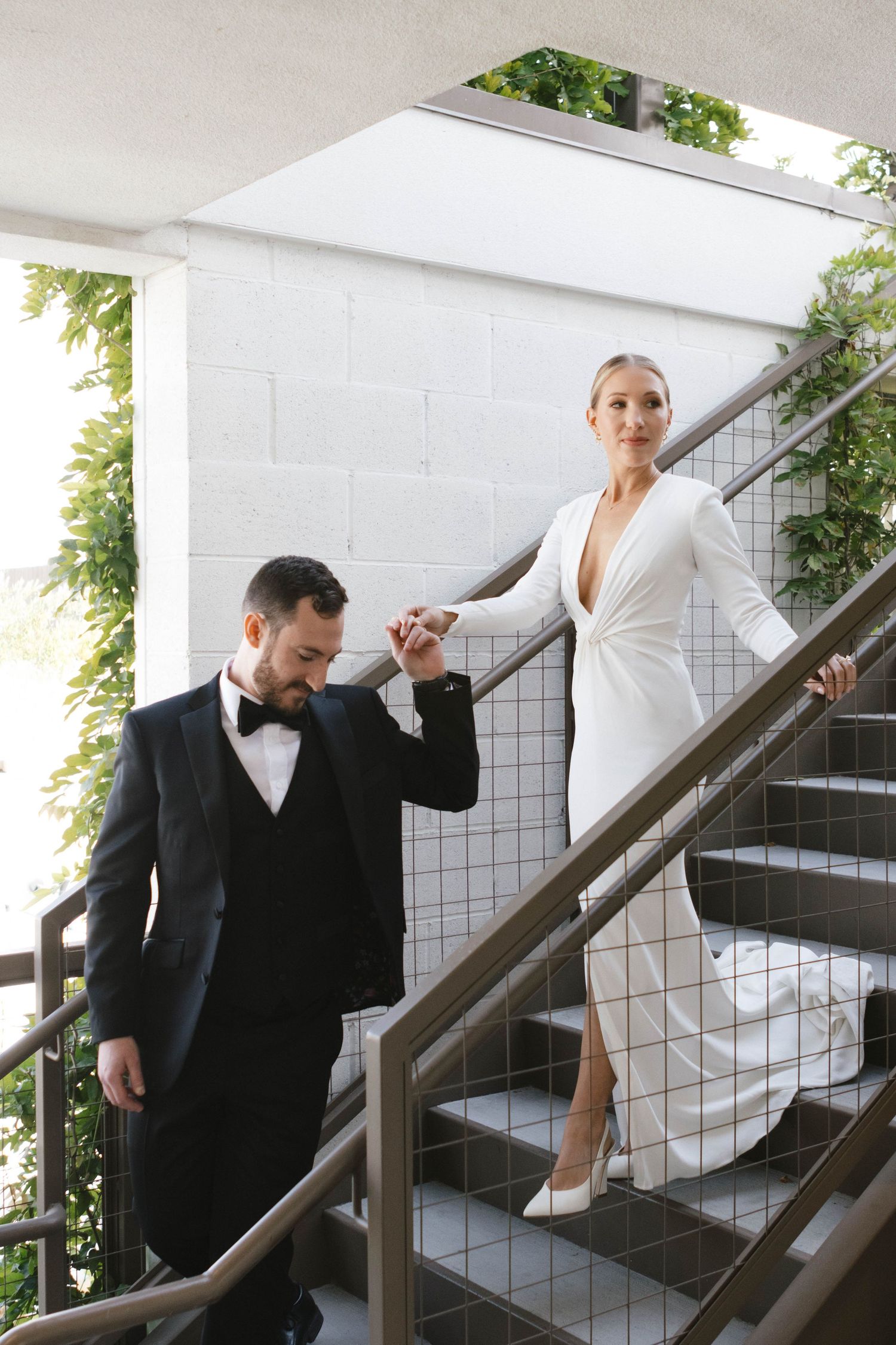 Two people in formal attire pose on a staircase with white tiled walls in a creative photoshoot sequence.