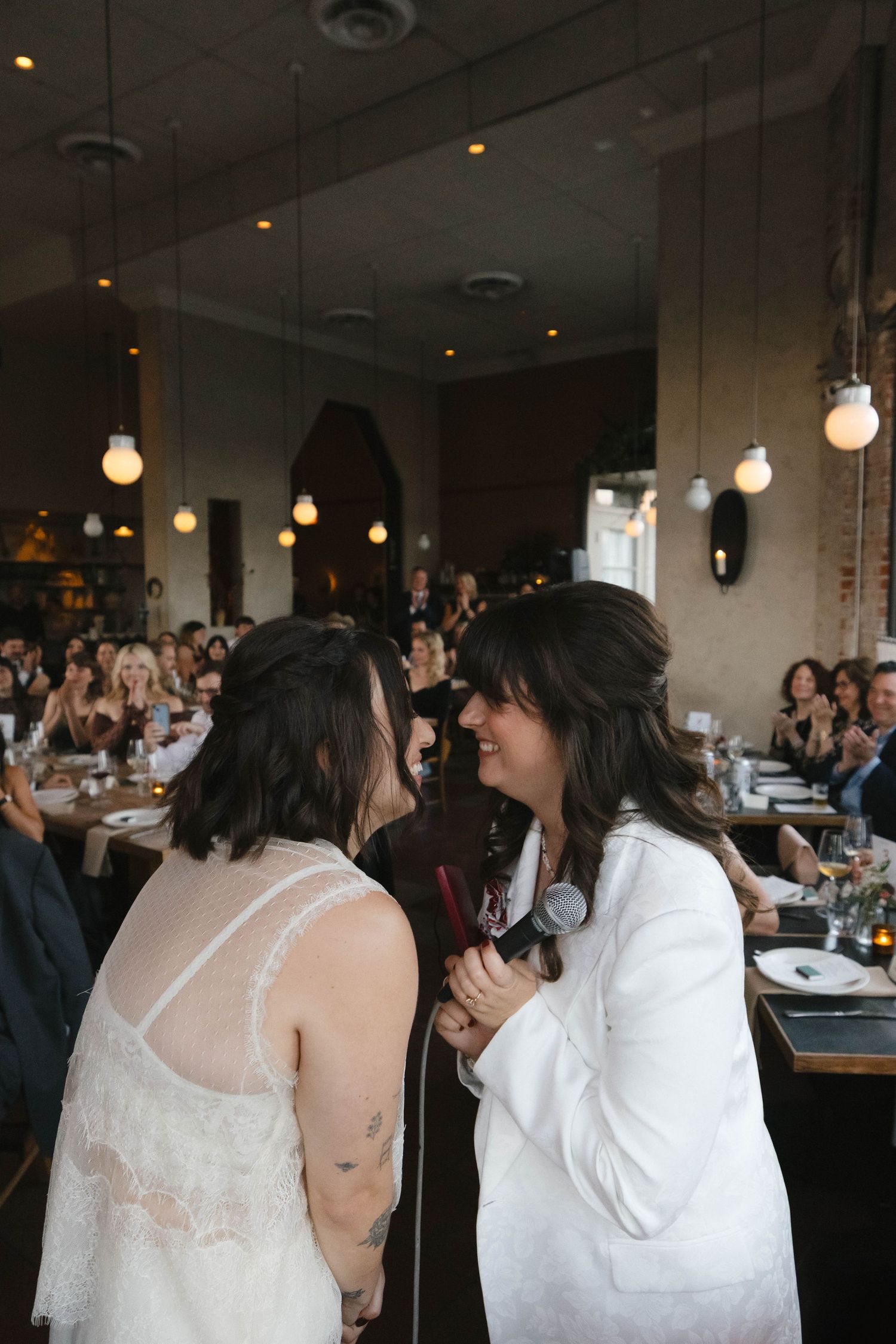 A romantic wedding celebration in a modern restaurant space with hanging light bulbs and guests gathered at tables.