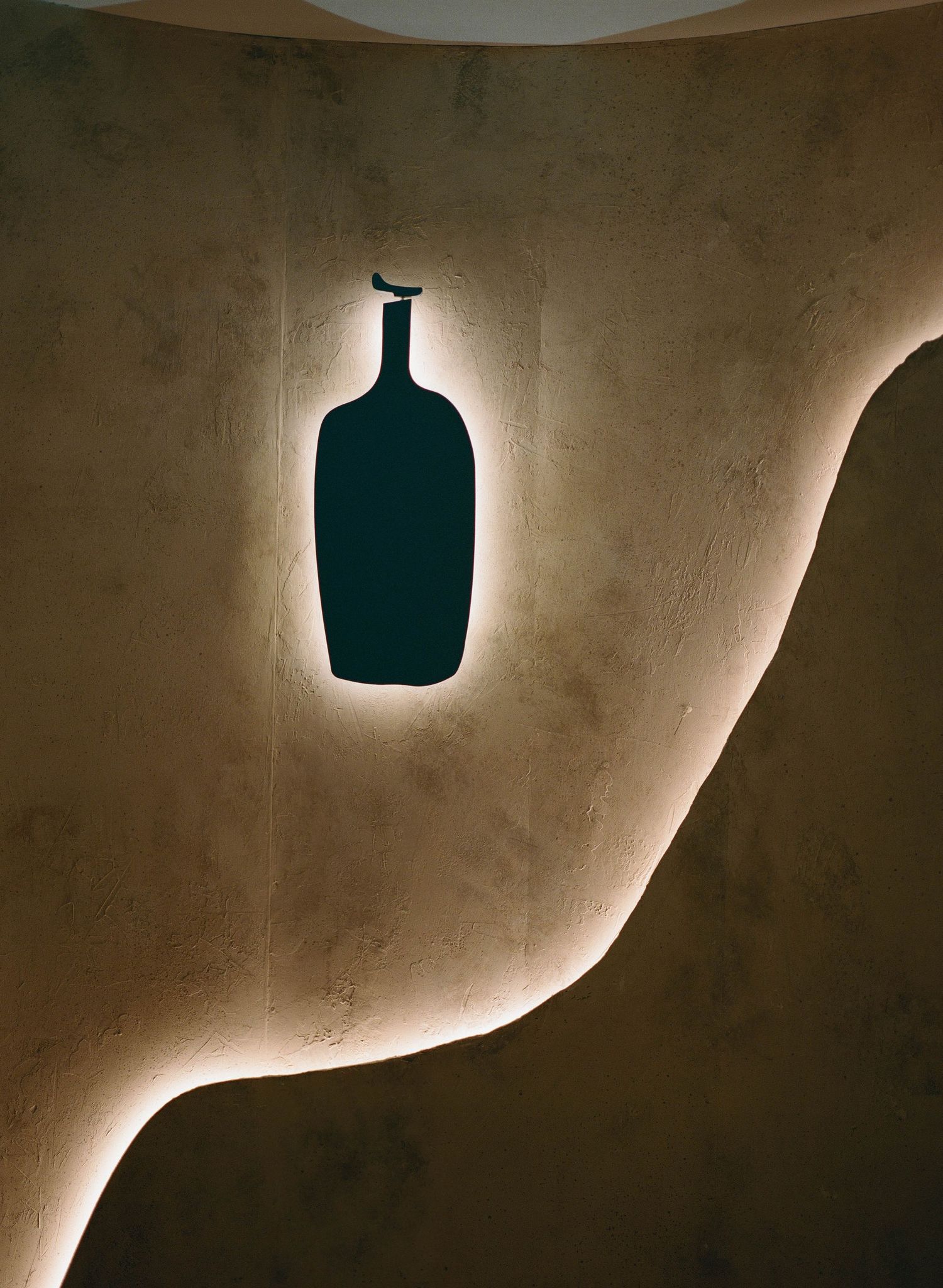 Illuminated bottle silhouette wall art with warm LED strip lighting on textured beige wall in modern interior design.