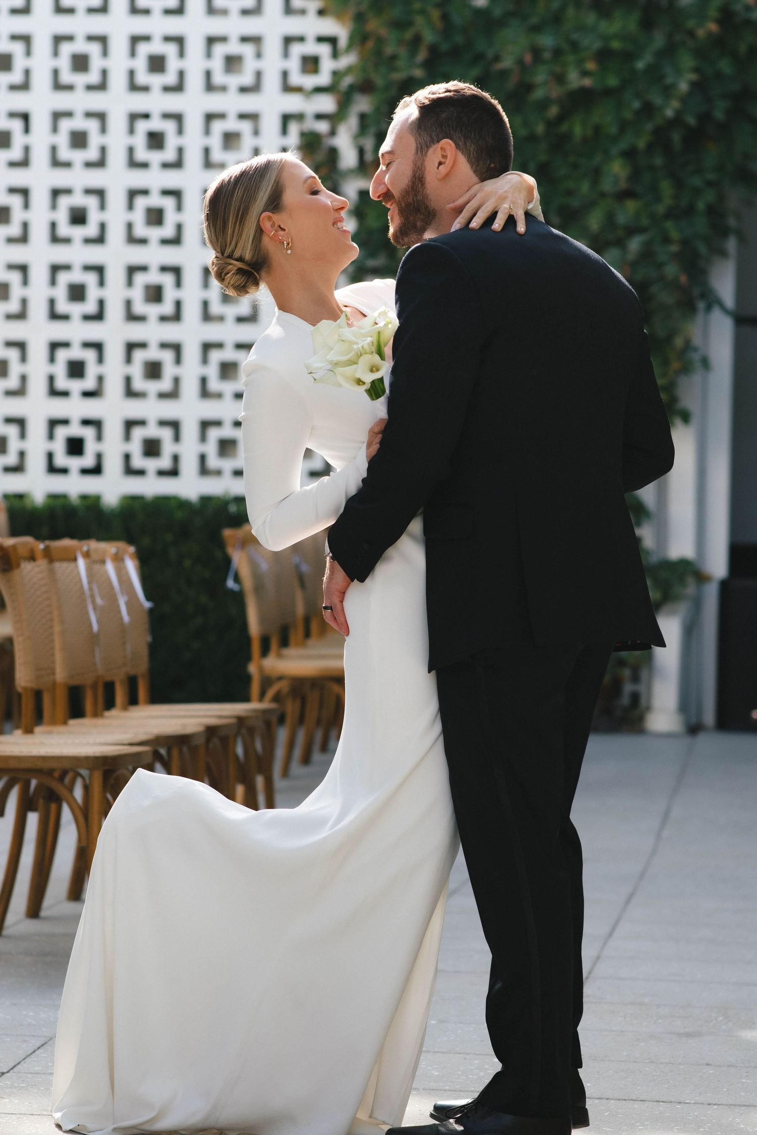 A couple in formal attire dancing together on an outdoor patio with geometric wall patterns.