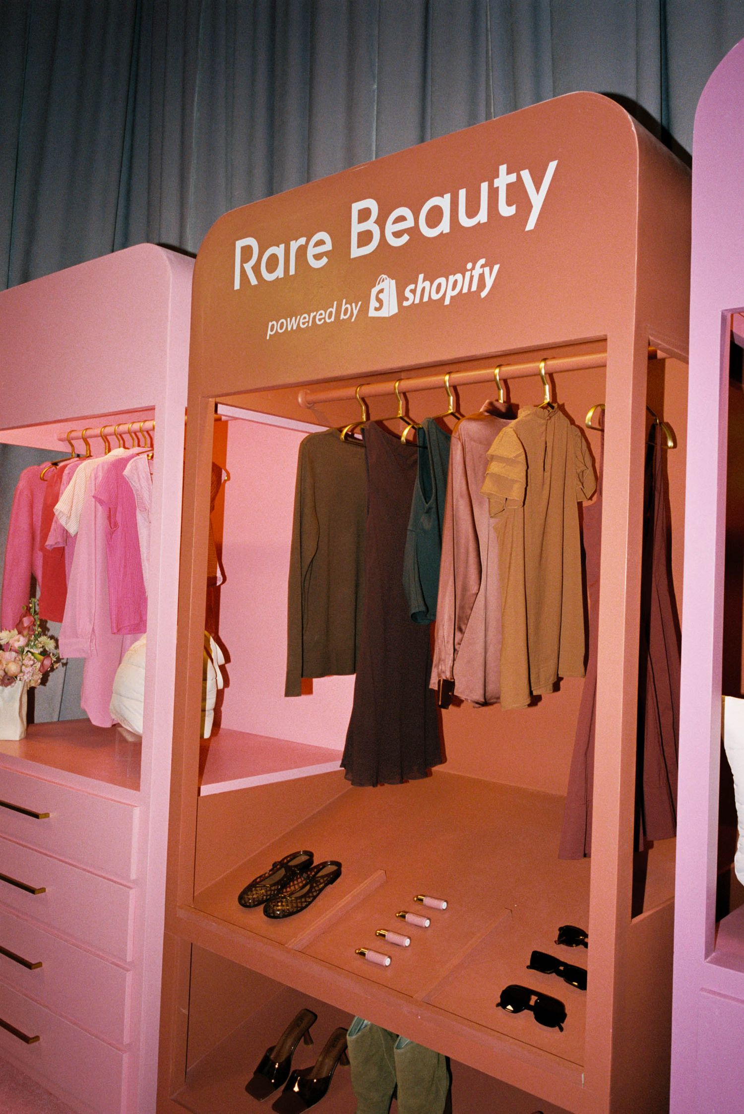 Pink-tinted retail space with clothing displayed on minimalist wall-mounted racks.