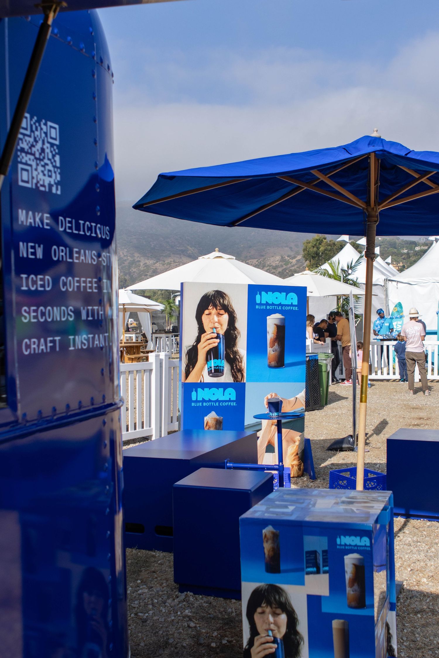 Blue branded coffee stand with promotional displays and umbrellas at outdoor event.