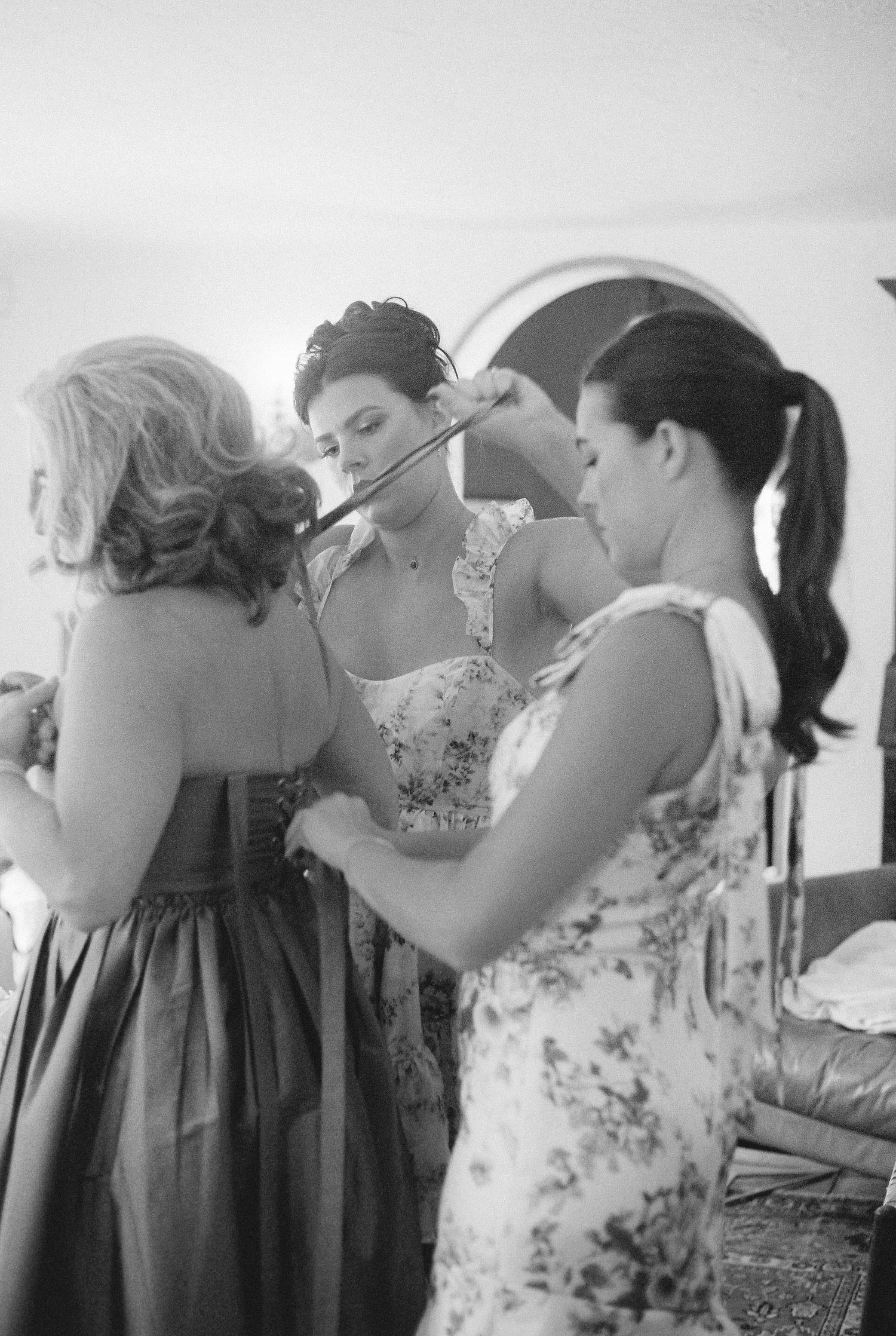 Group of bridesmaids in floral dresses helping with wedding preparations.